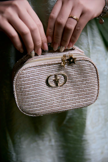 Woman holding a small, sparkly handbag with a gold logo.