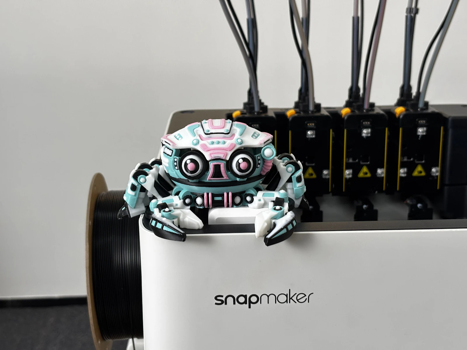 Small colourful robot on a 3D printer beside toolheads