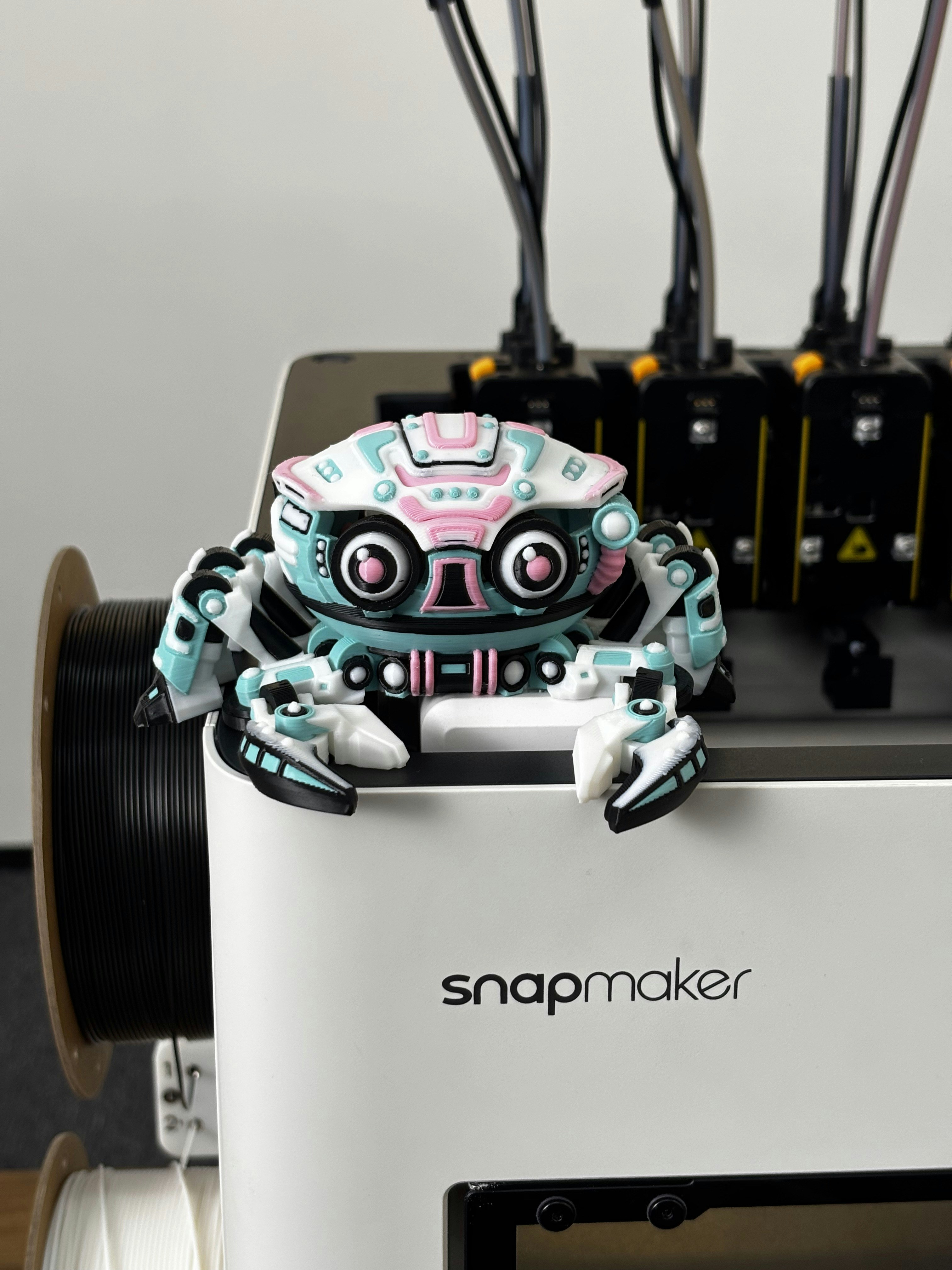 A colorful robot toy sits on a 3D printer.