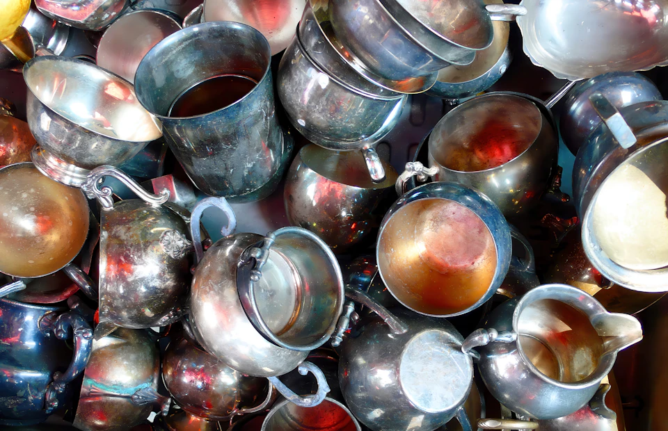 Metallic objects, mostly silver and gold, scattered across a table or shelf in various arrangements