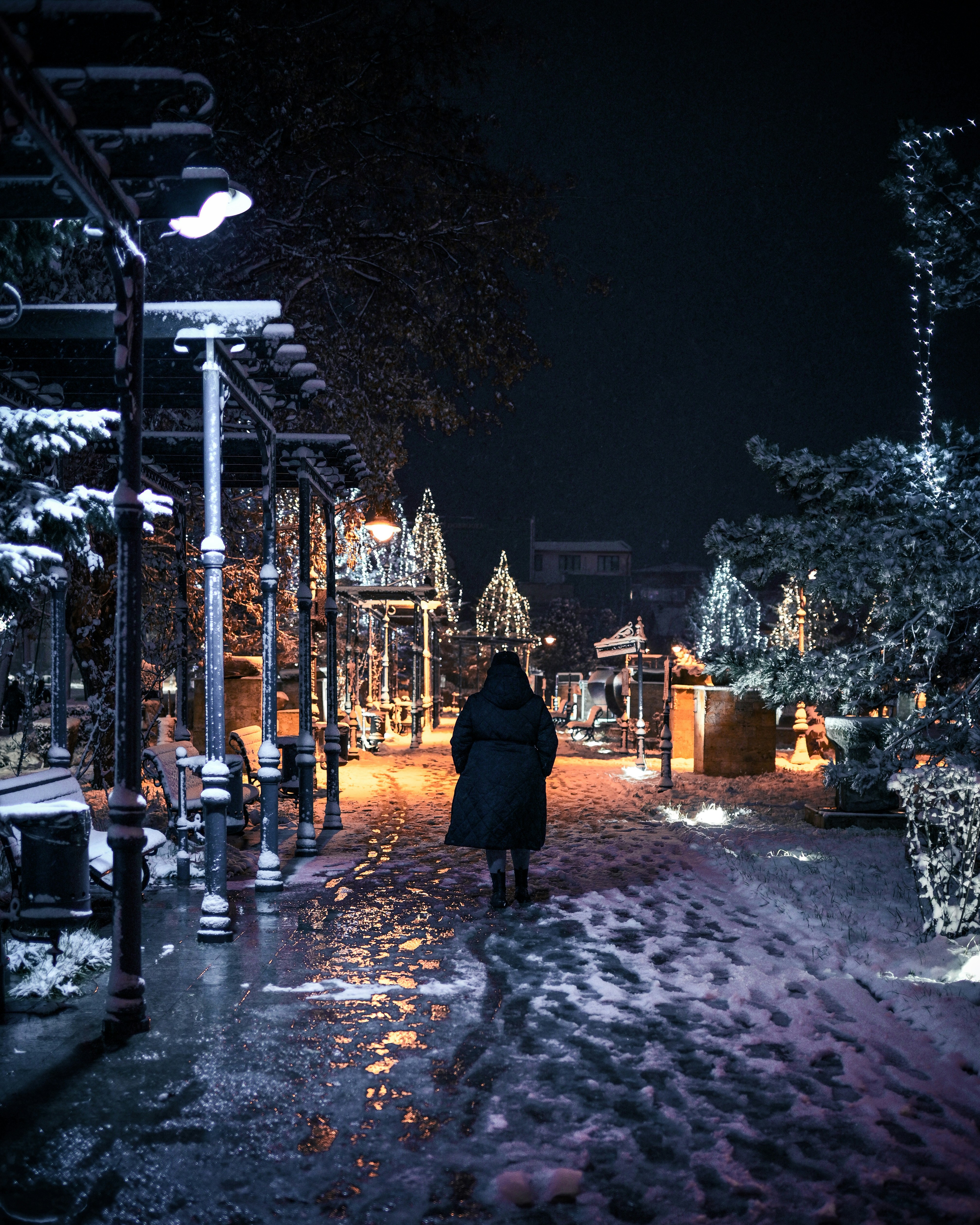 Person walks through a snowy, decorated street at night.