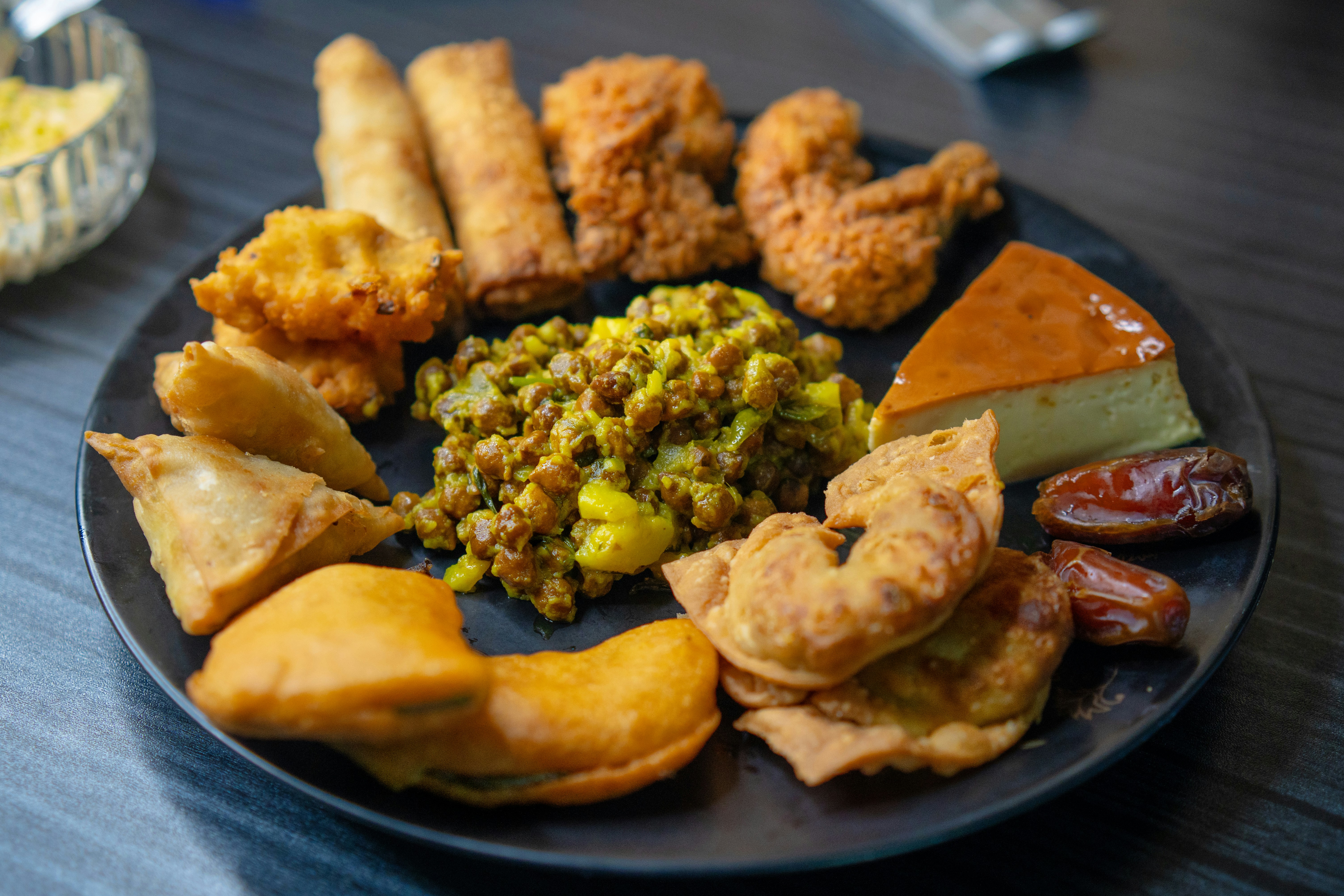 A black plate filled with assorted fried snacks and dates