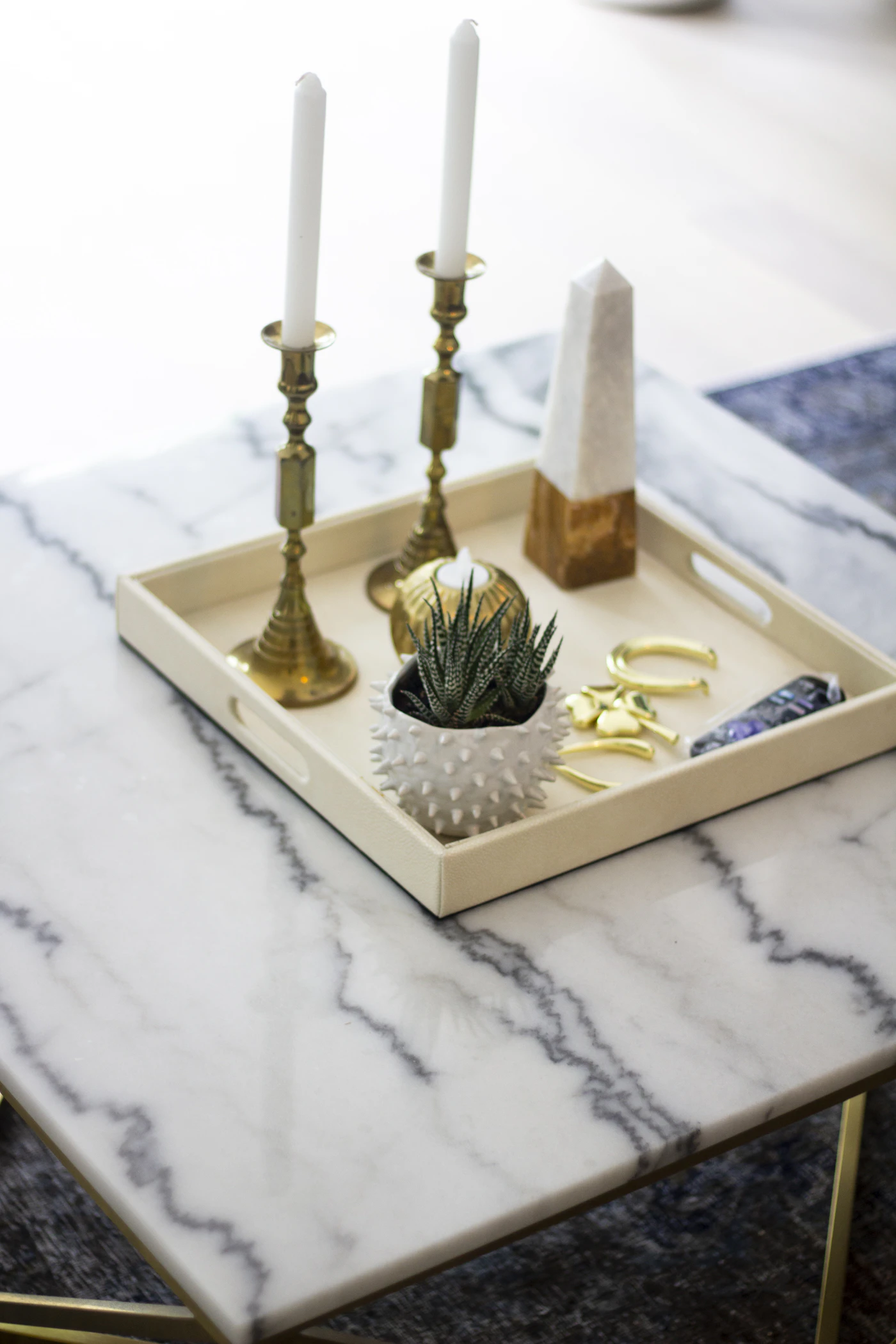 Decorative tray with candle holders and styling objects on a marble table for entryway console organization