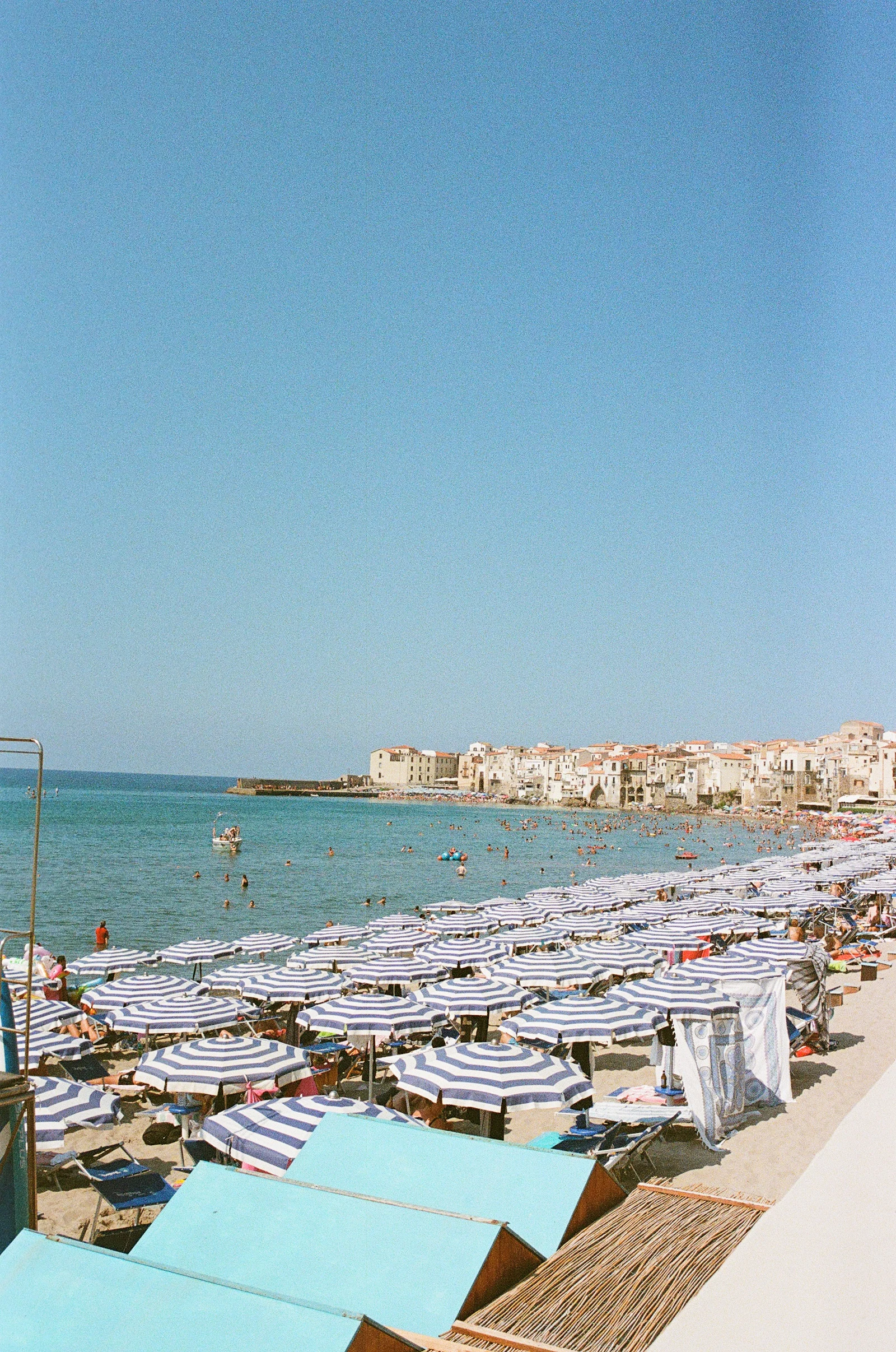 Rows of blue and white striped parasols on a beach below a town.