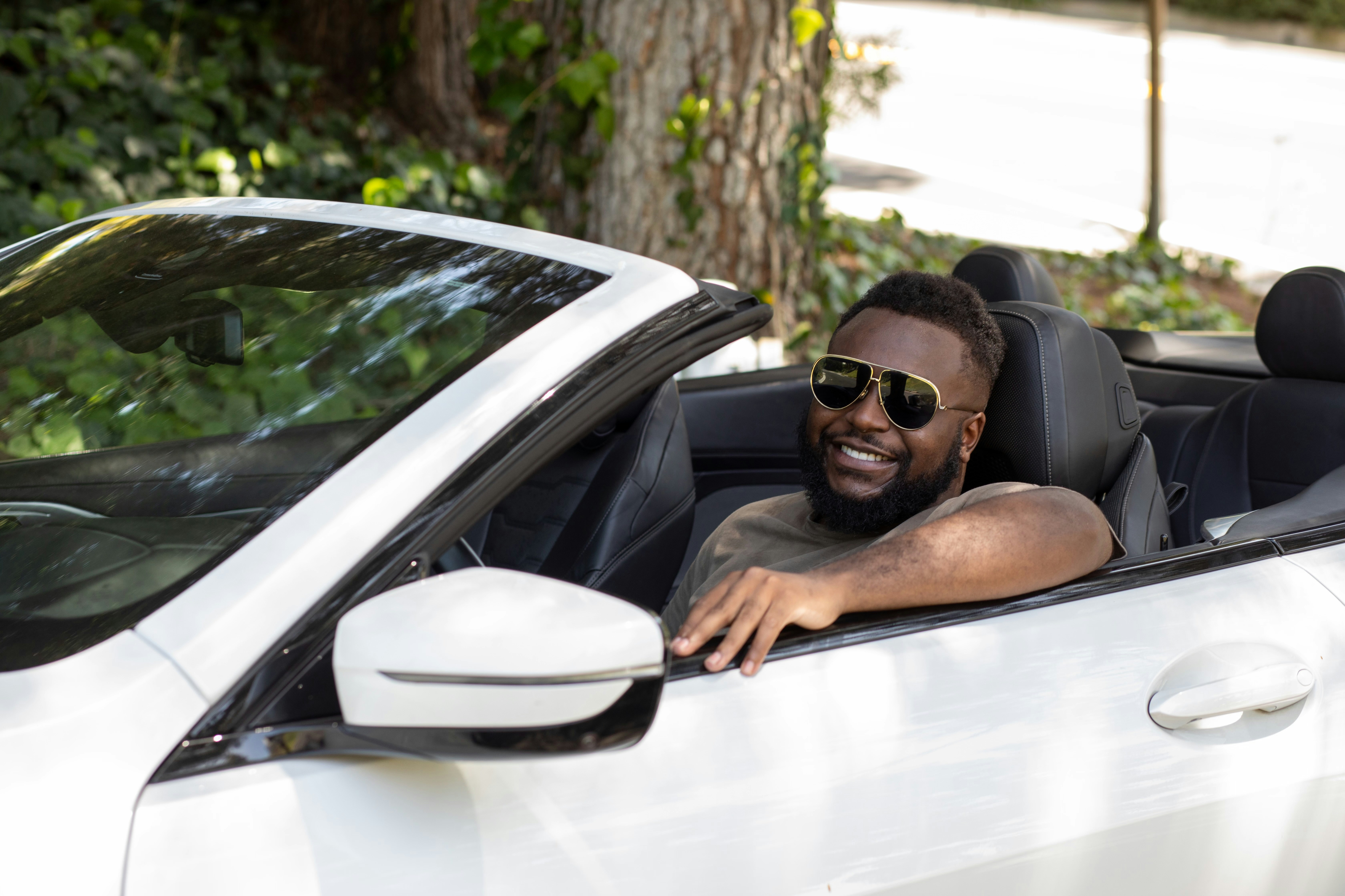 A smiling man in sunglasses drives a white convertible car