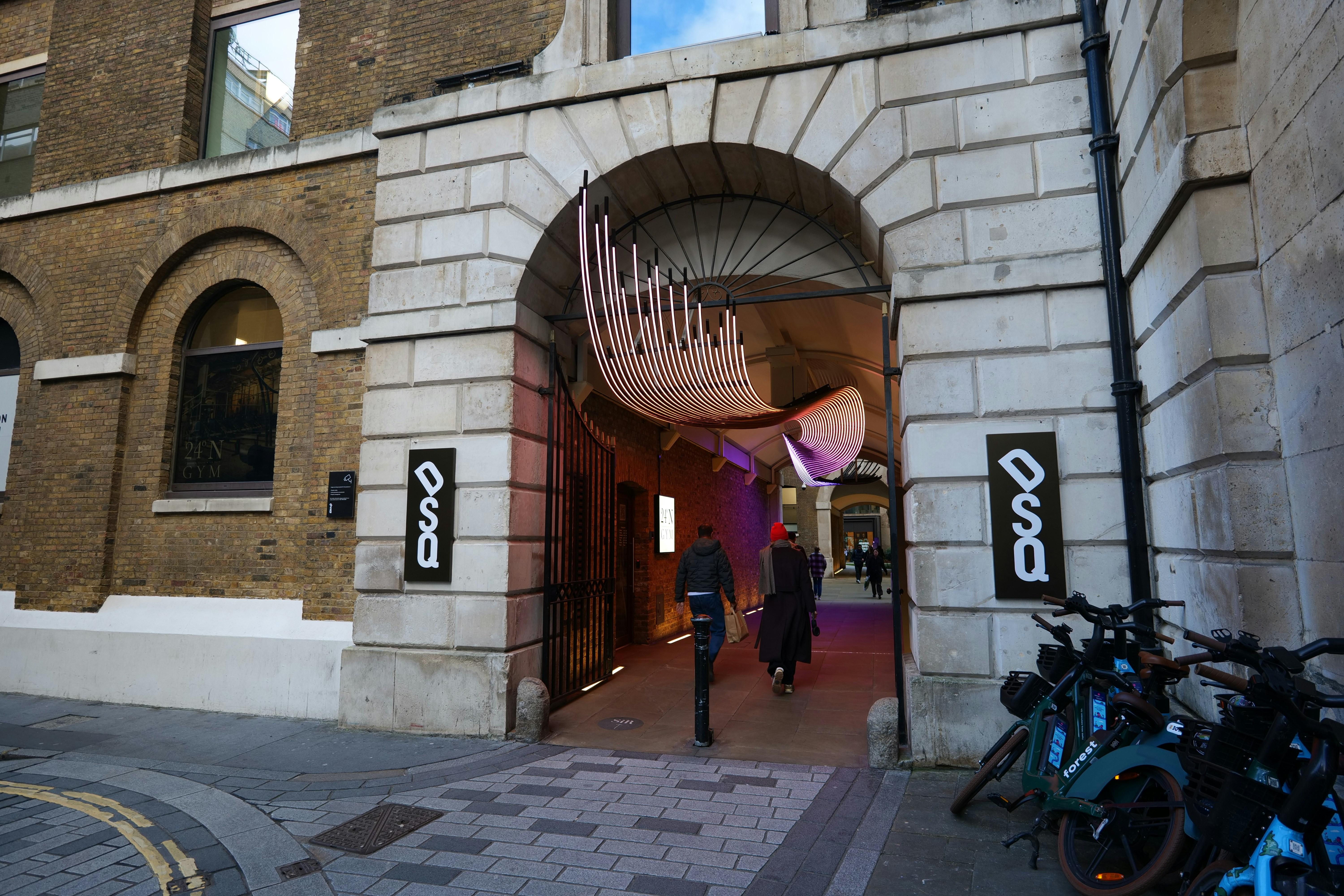 People walk through a stone archway with art installation.