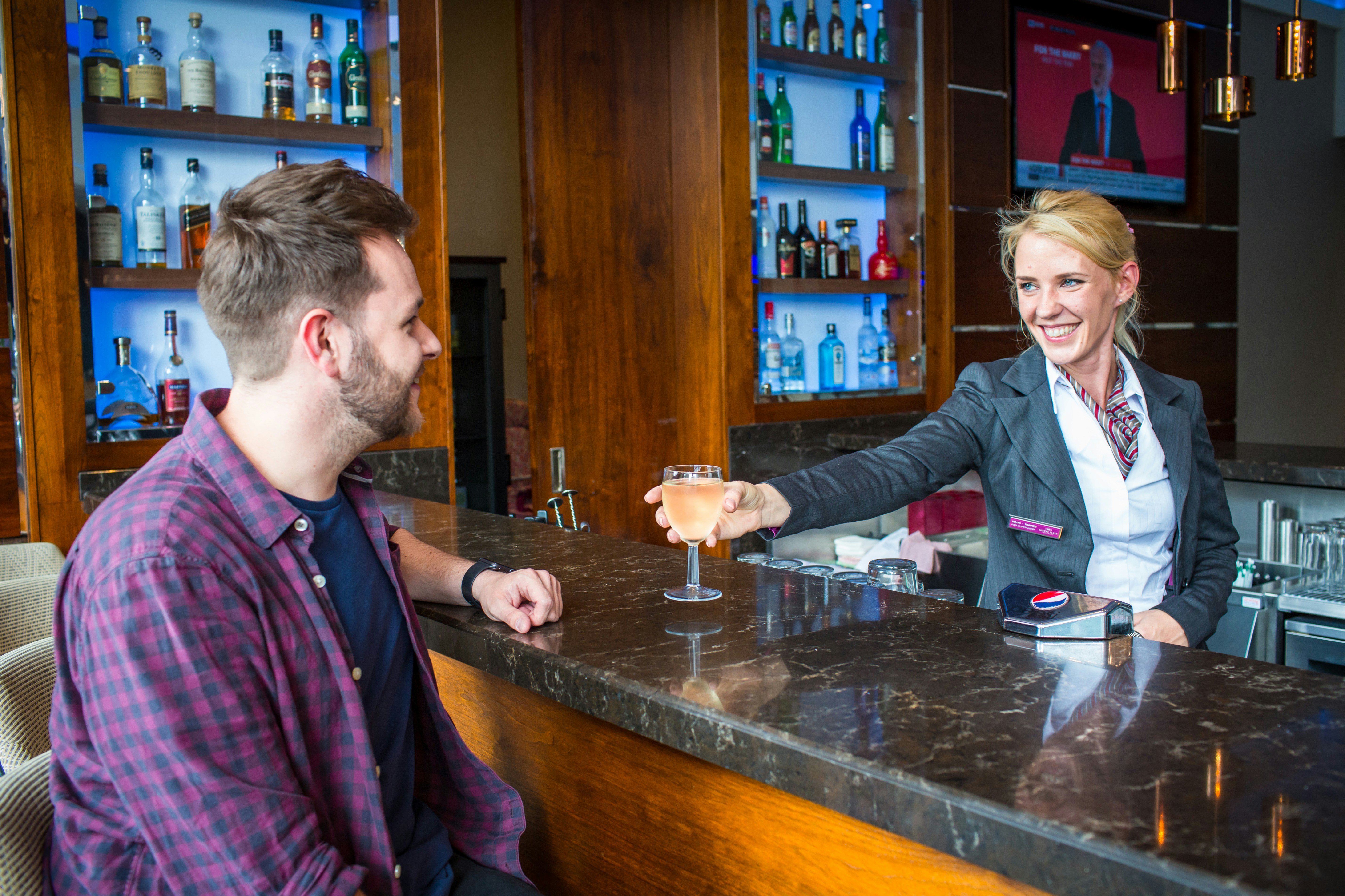 Bartender serves a drink to a customer at bar.