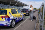 Woman with suitcase walks by a yellow taxi at airport
