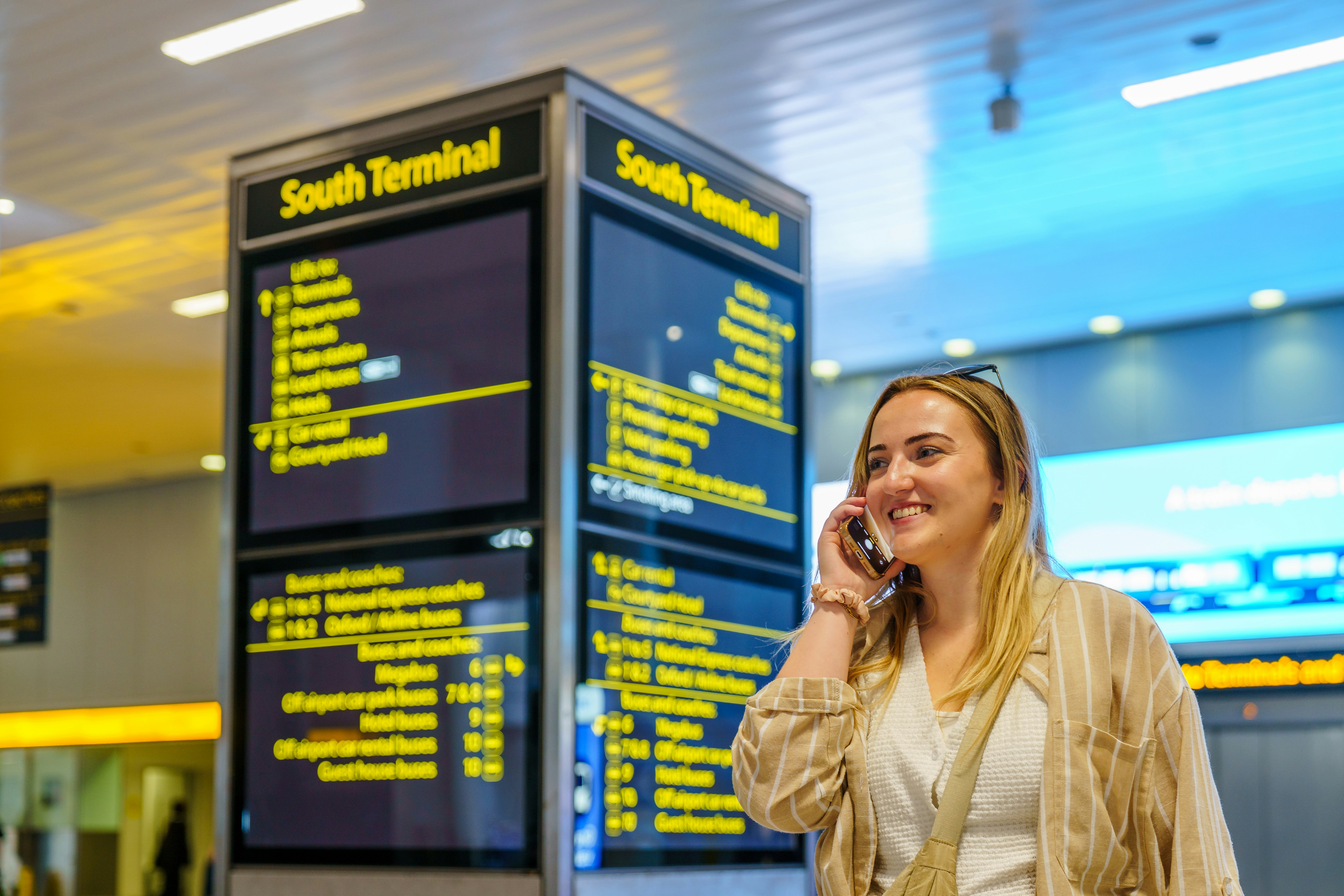 Woman talking on a phone near an airport departure board