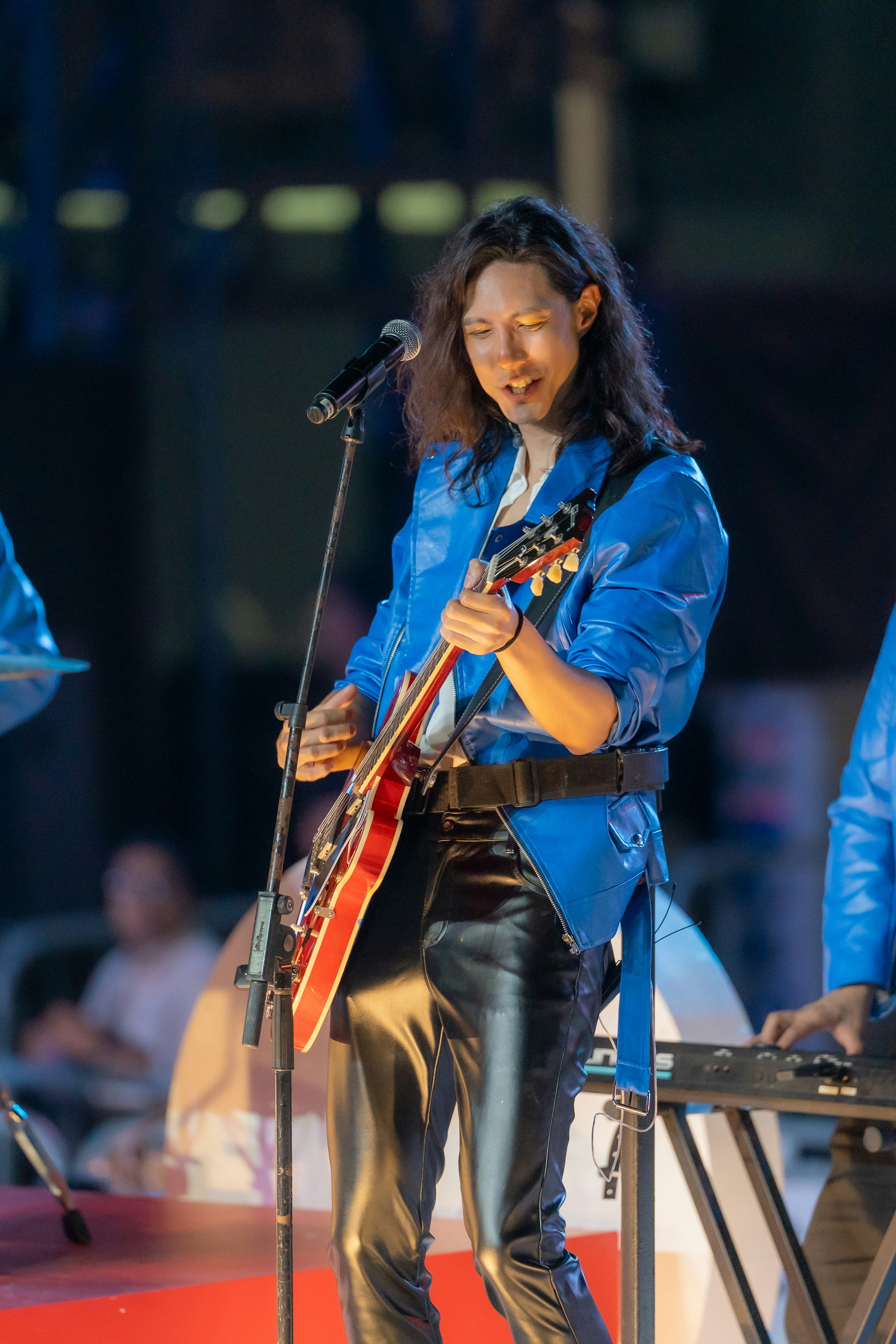 A musician plays a red electric guitar on stage.