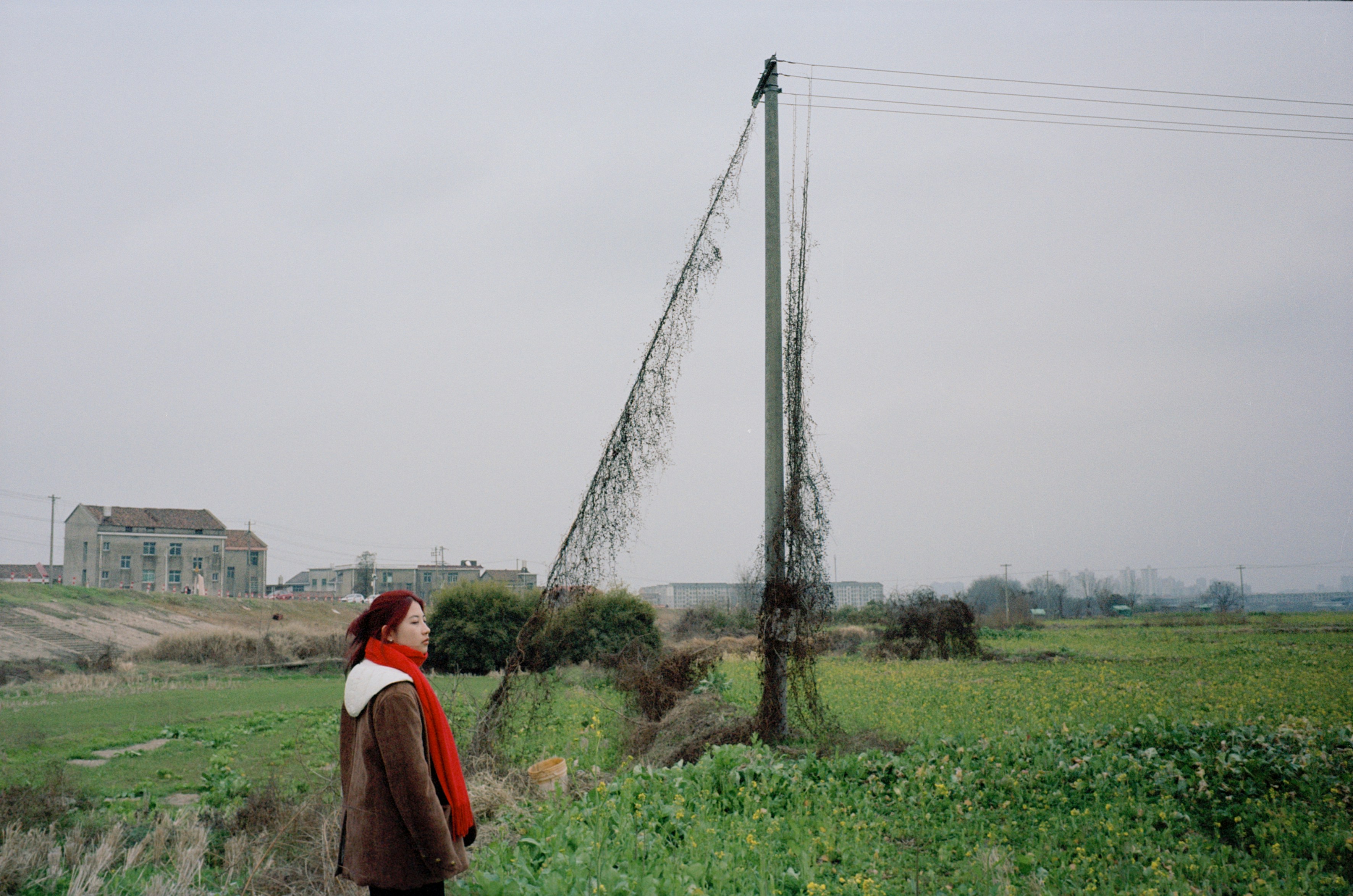Woman in red scarf stands in a field.