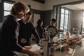 Community group gathered around a coffee machine in a kitchen.