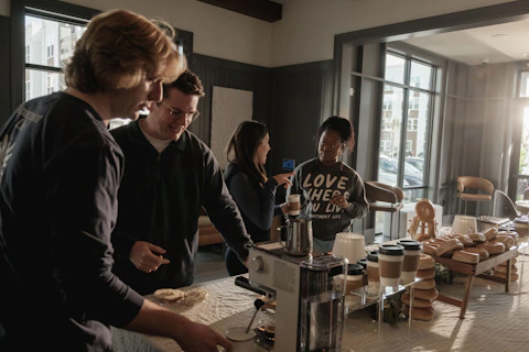 Community group gathered around a coffee machine in a kitchen.
