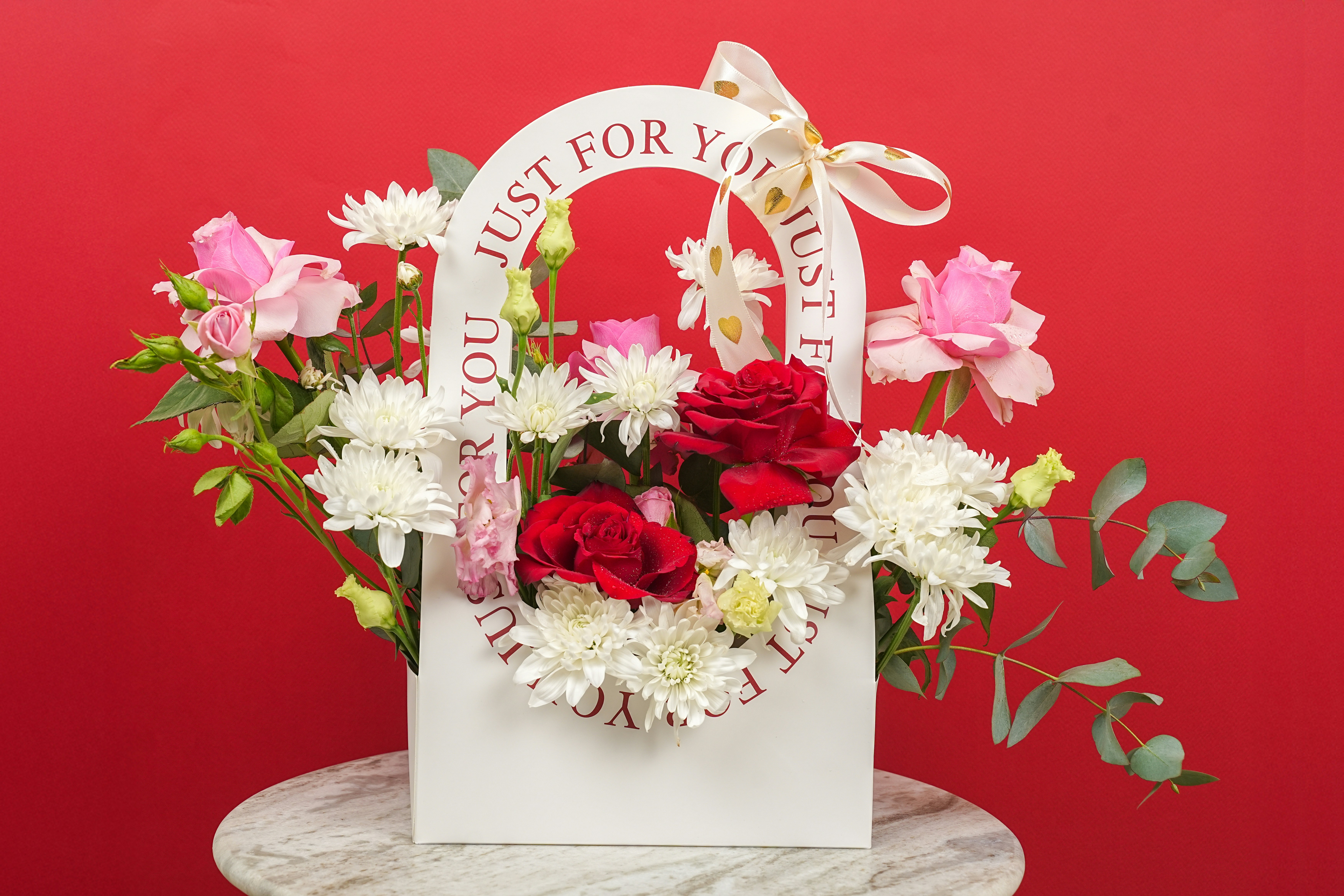 A floral arrangement in a white bag with red background