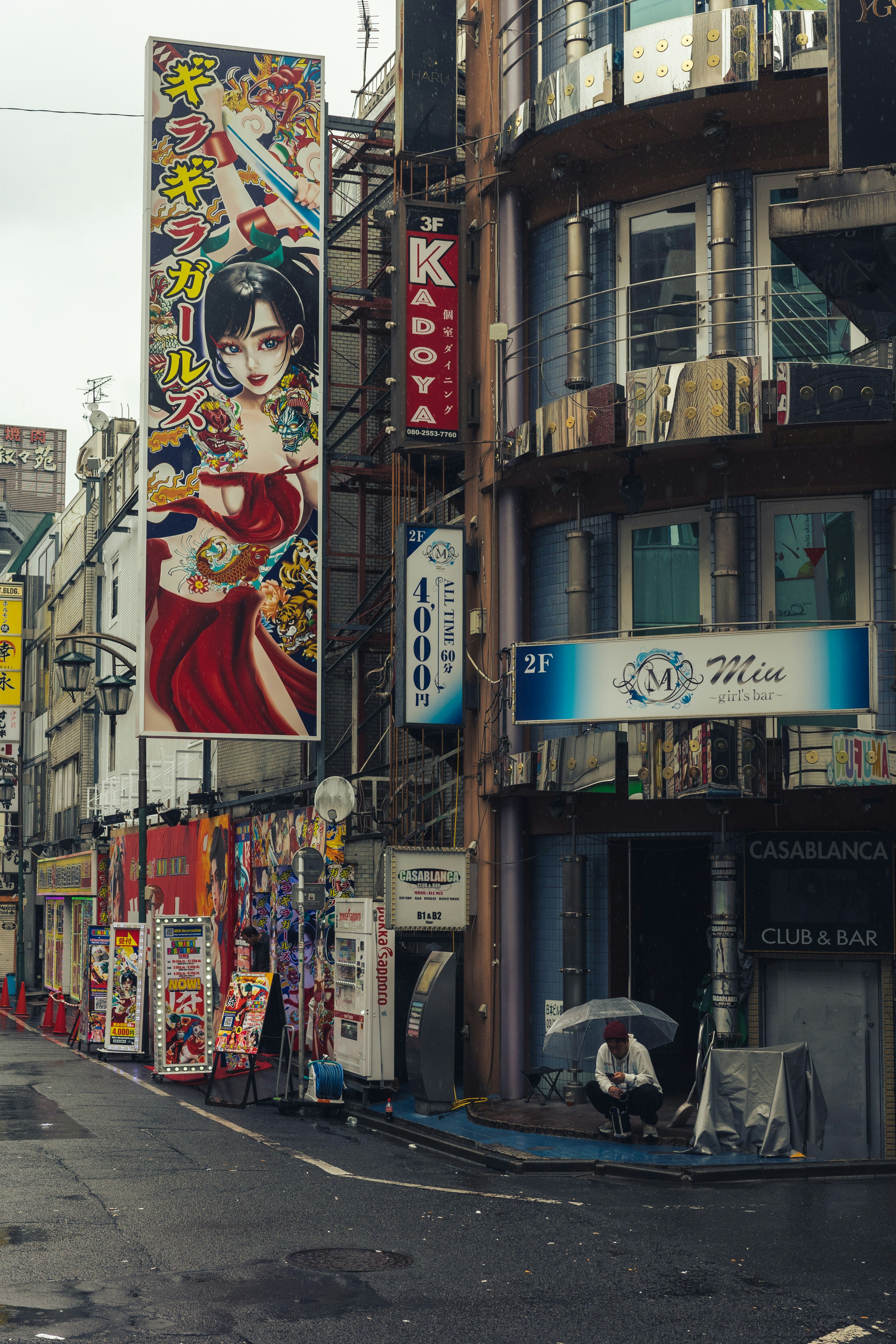 A person sits under an umbrella on a street.
