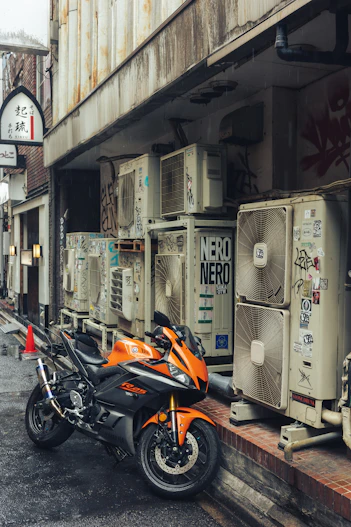 Orange motorcycle parked beside air conditioning units