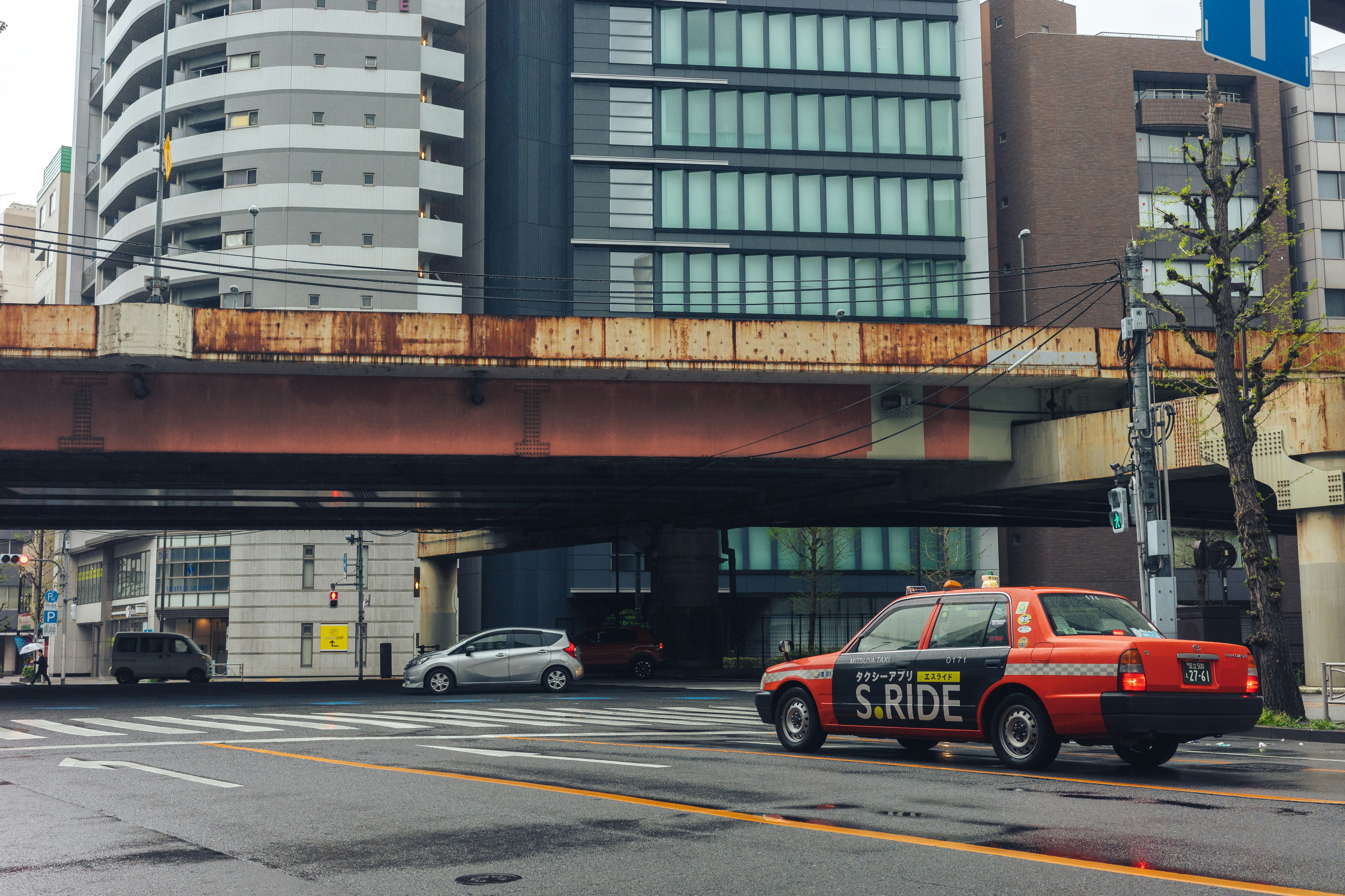 Red taxi drives under a bridge in a city.