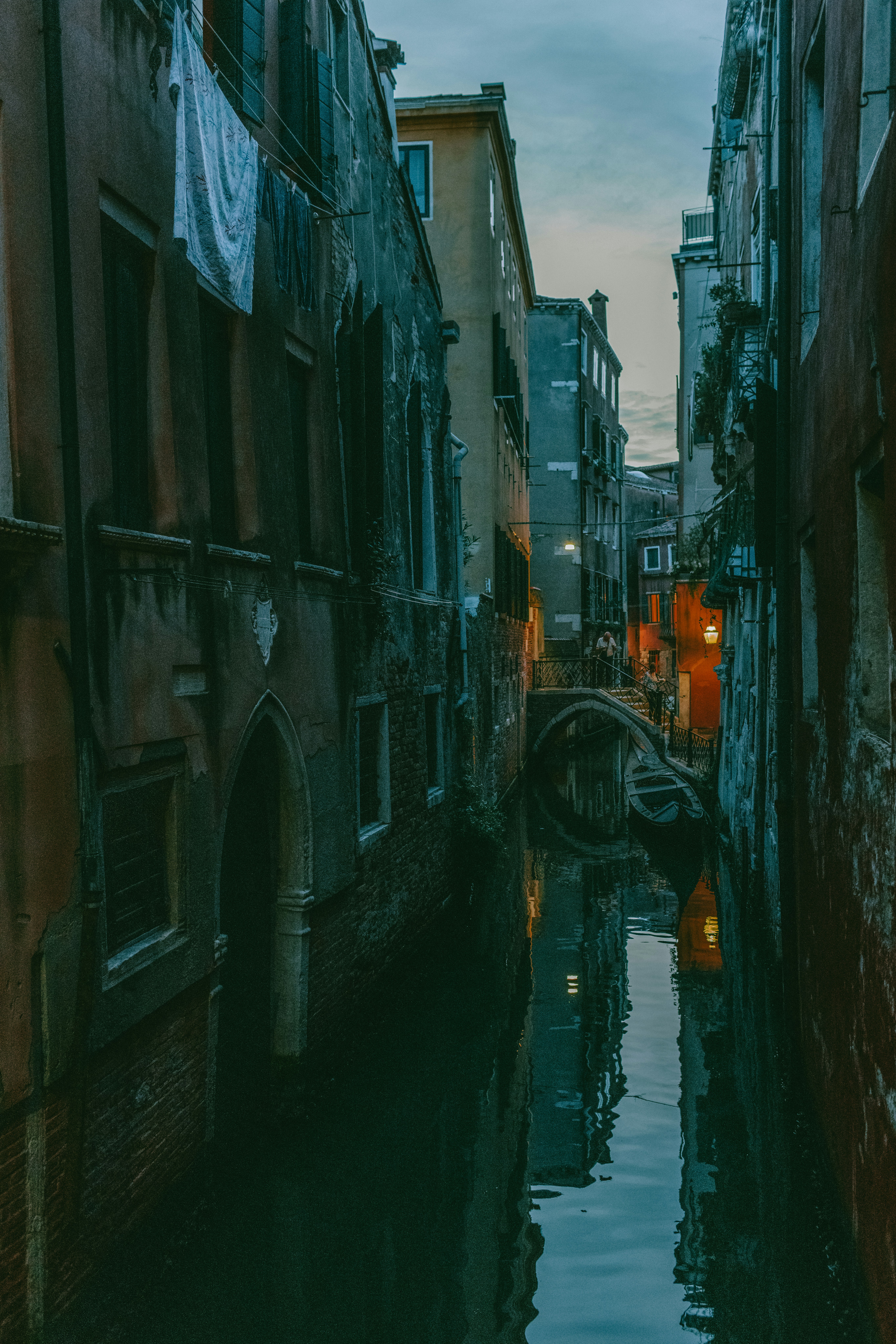 Narrow canal between old buildings in venice at dusk.