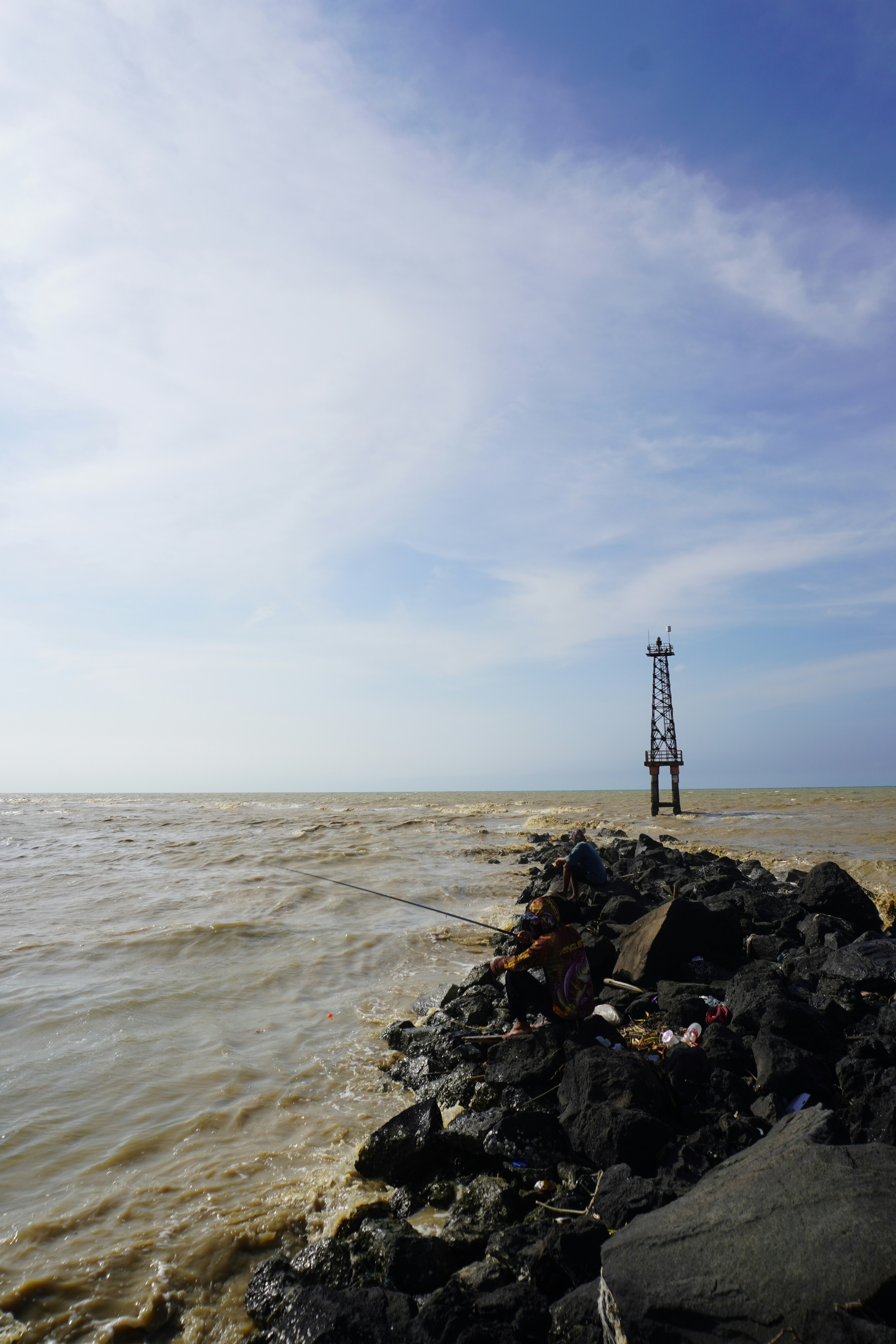 A tall metal tower stands in the choppy ocean water.