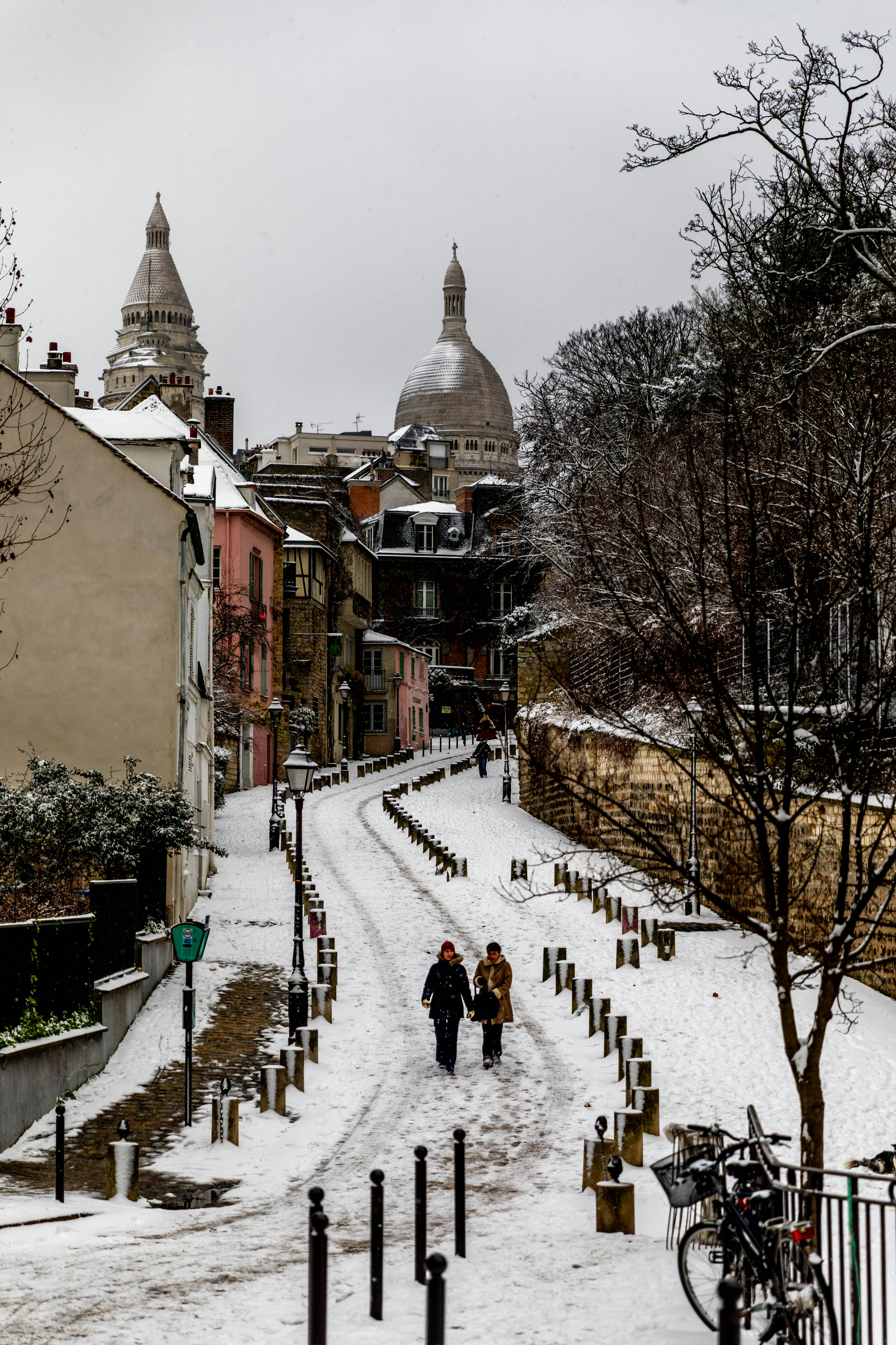 Two people walk up a snowy street in paris.