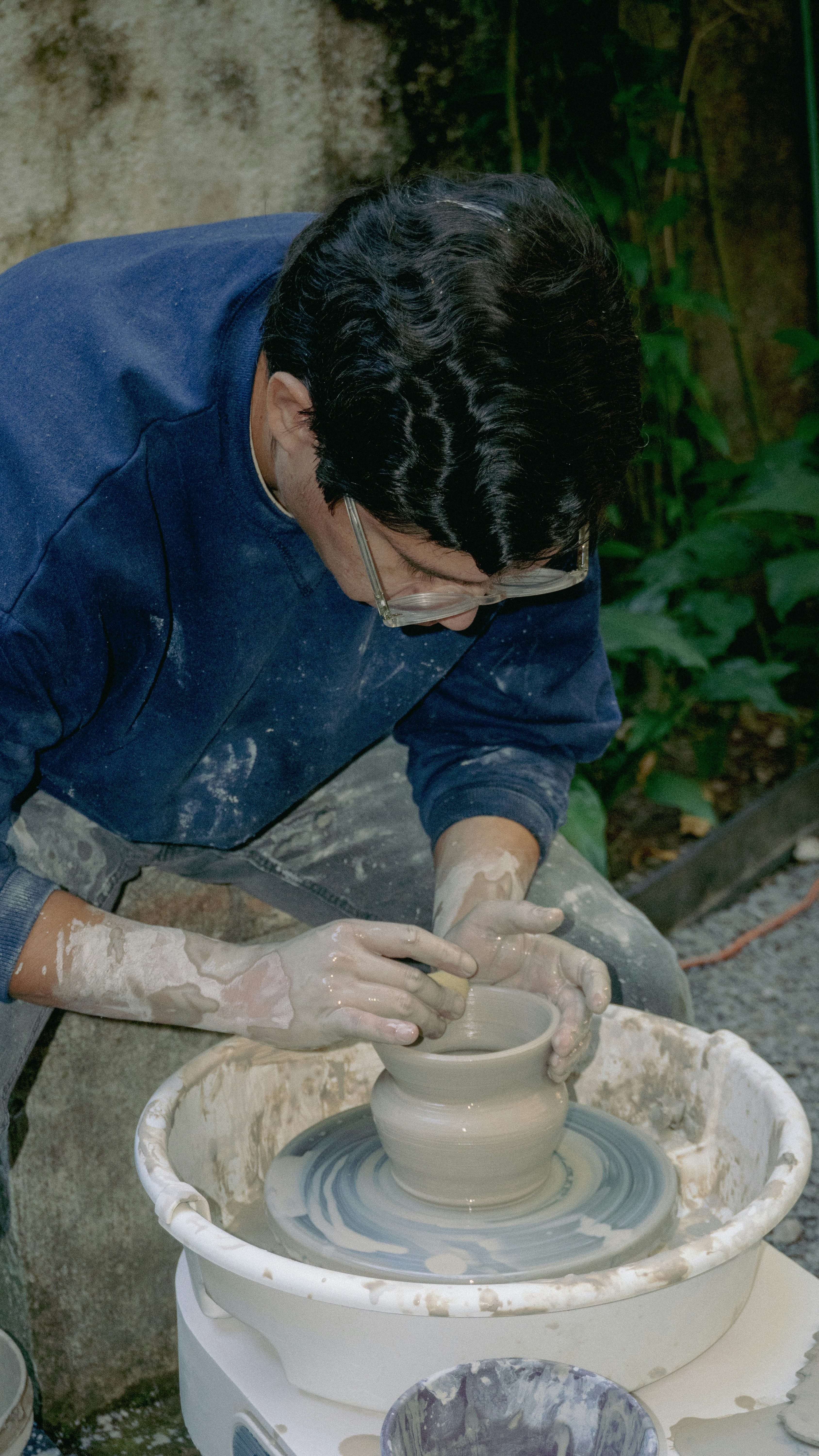 Potter shaping clay on a pottery wheel outdoors