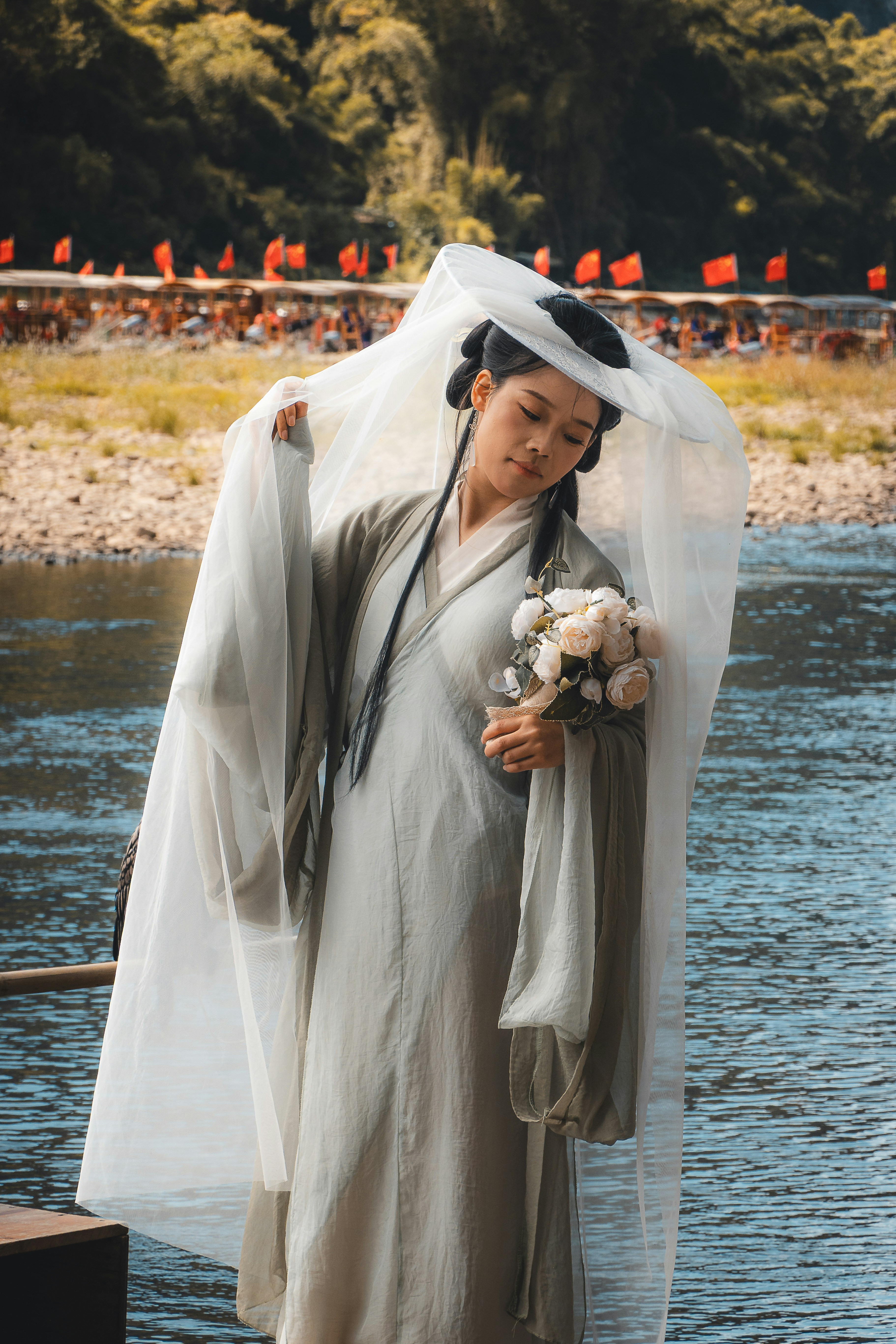 Woman in traditional chinese dress holds flowers by river