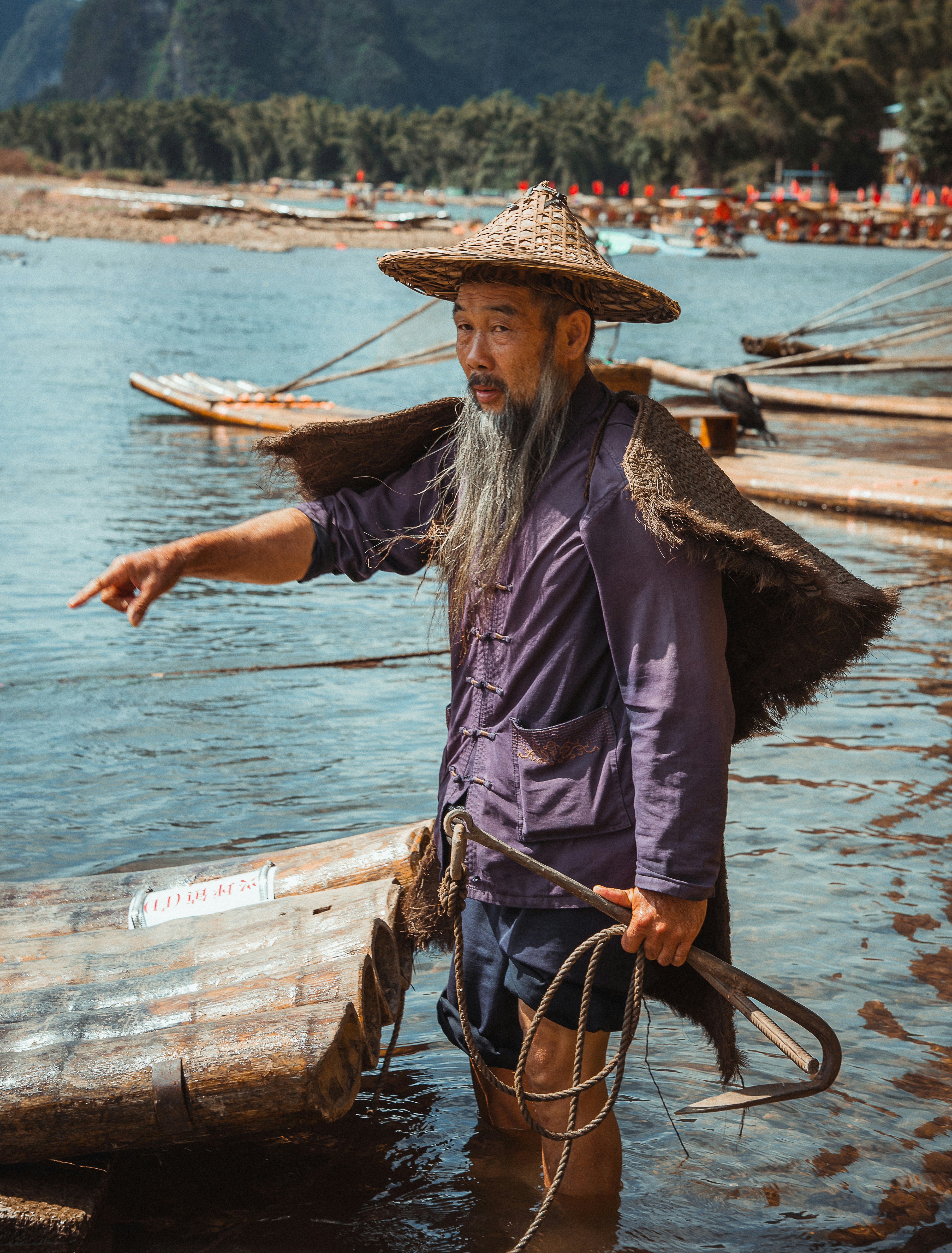 Elderly fisherman in traditional hat points ahead by river.