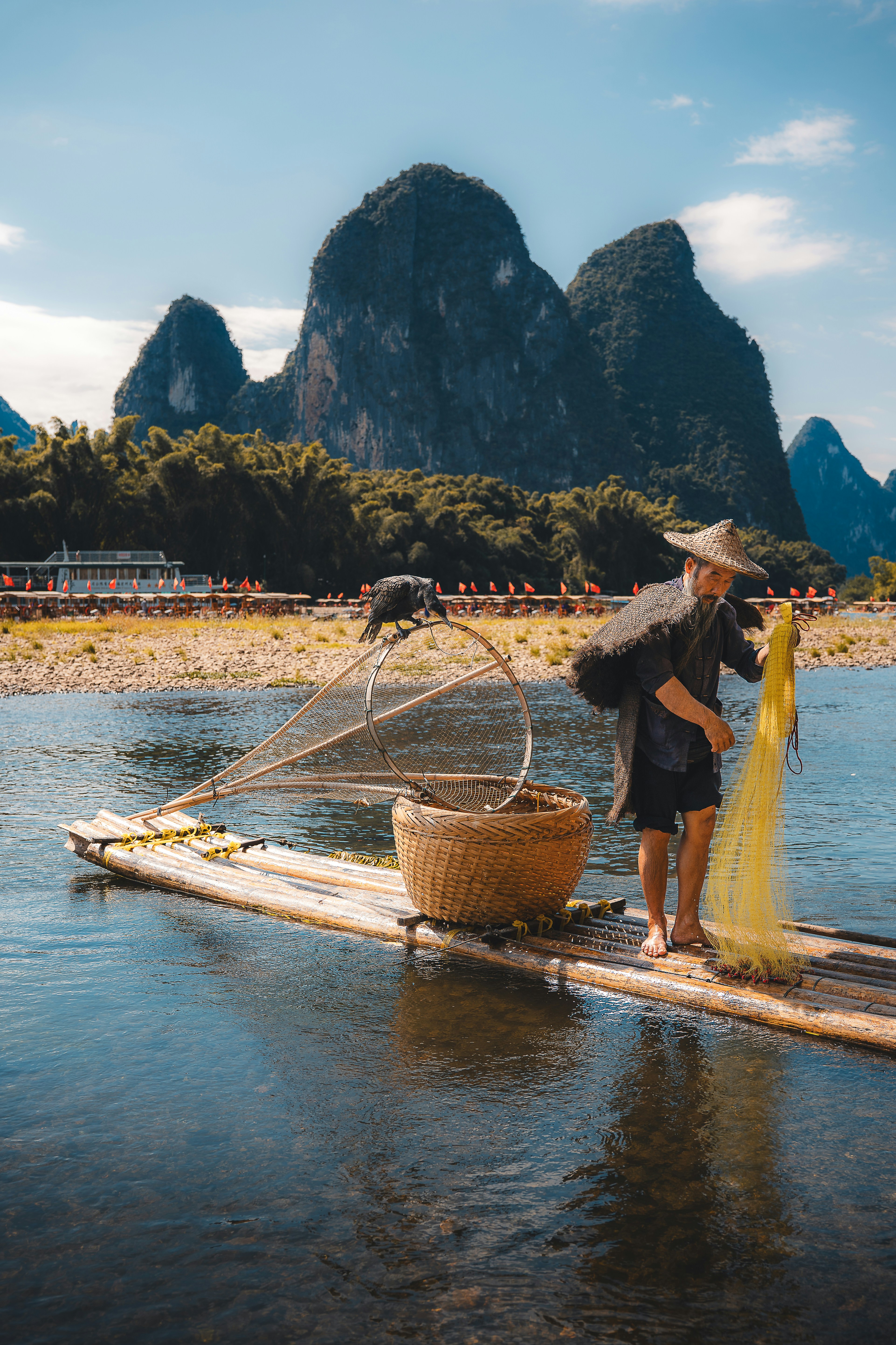 Fisherman with net on bamboo raft, karst mountains background.