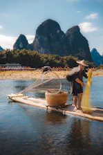 Fisherman with net on bamboo raft, karst mountains background.