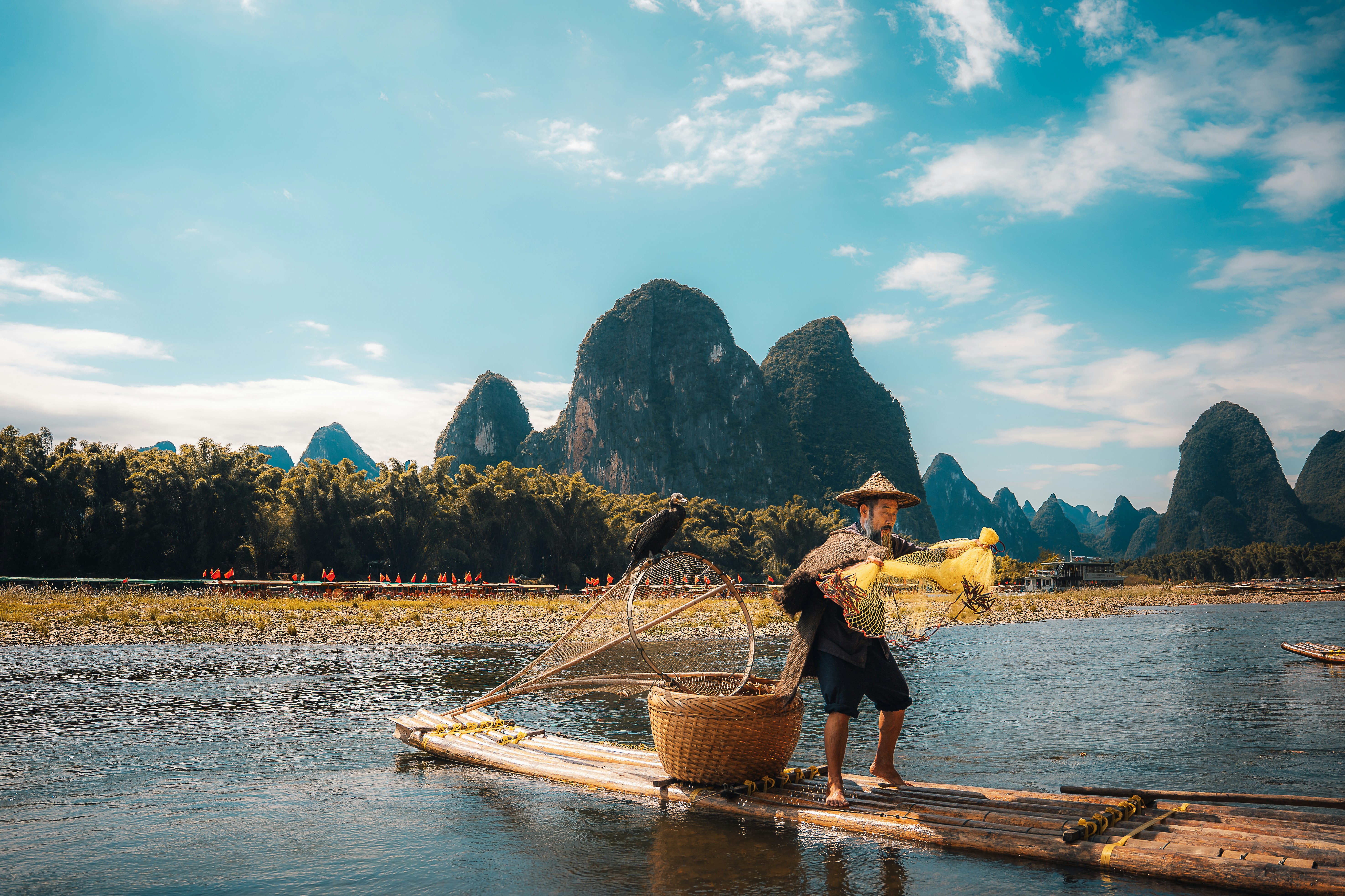 Fisherman on raft with cormorant and mountains