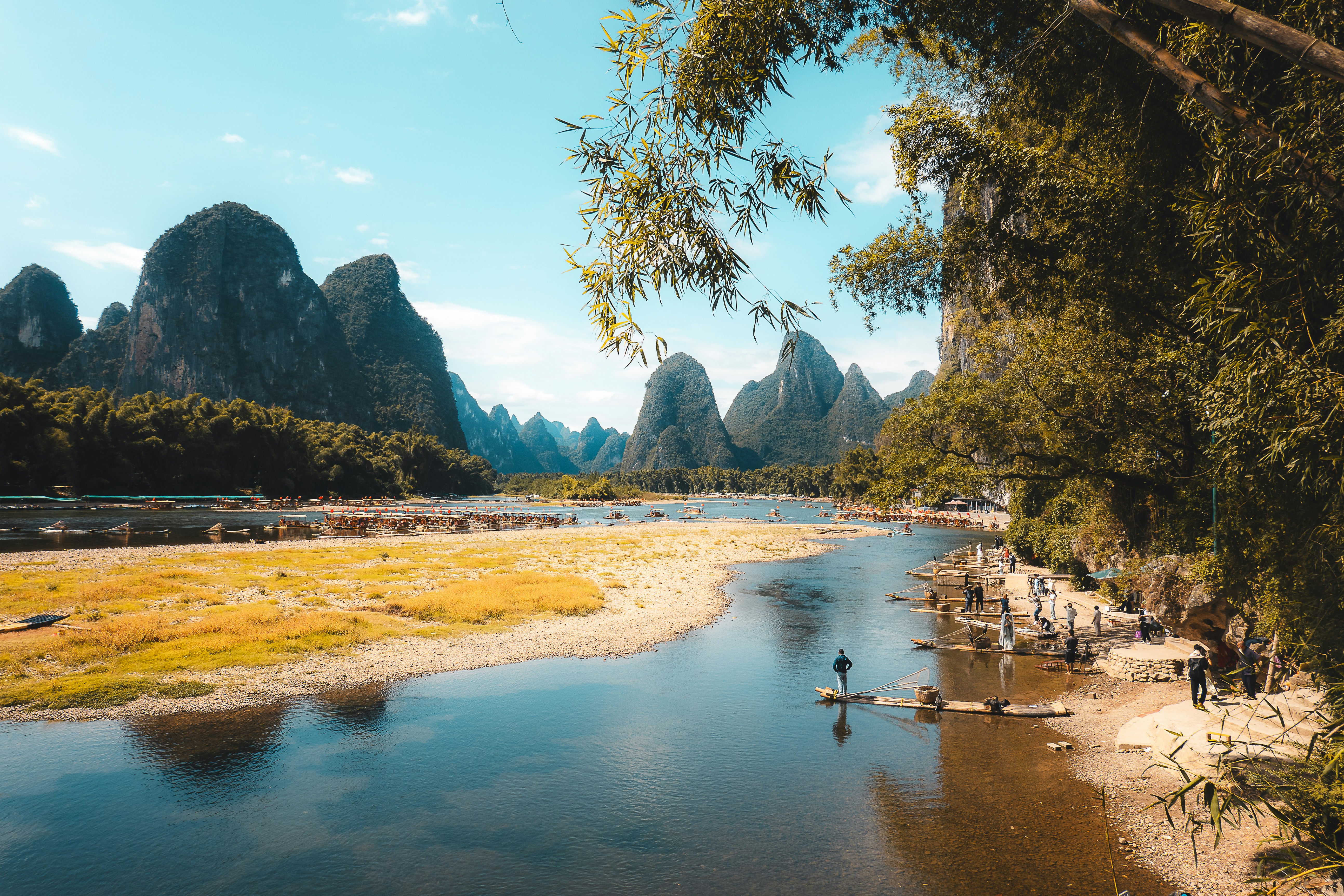 Karst mountains rise above a tranquil river with bamboo trees.