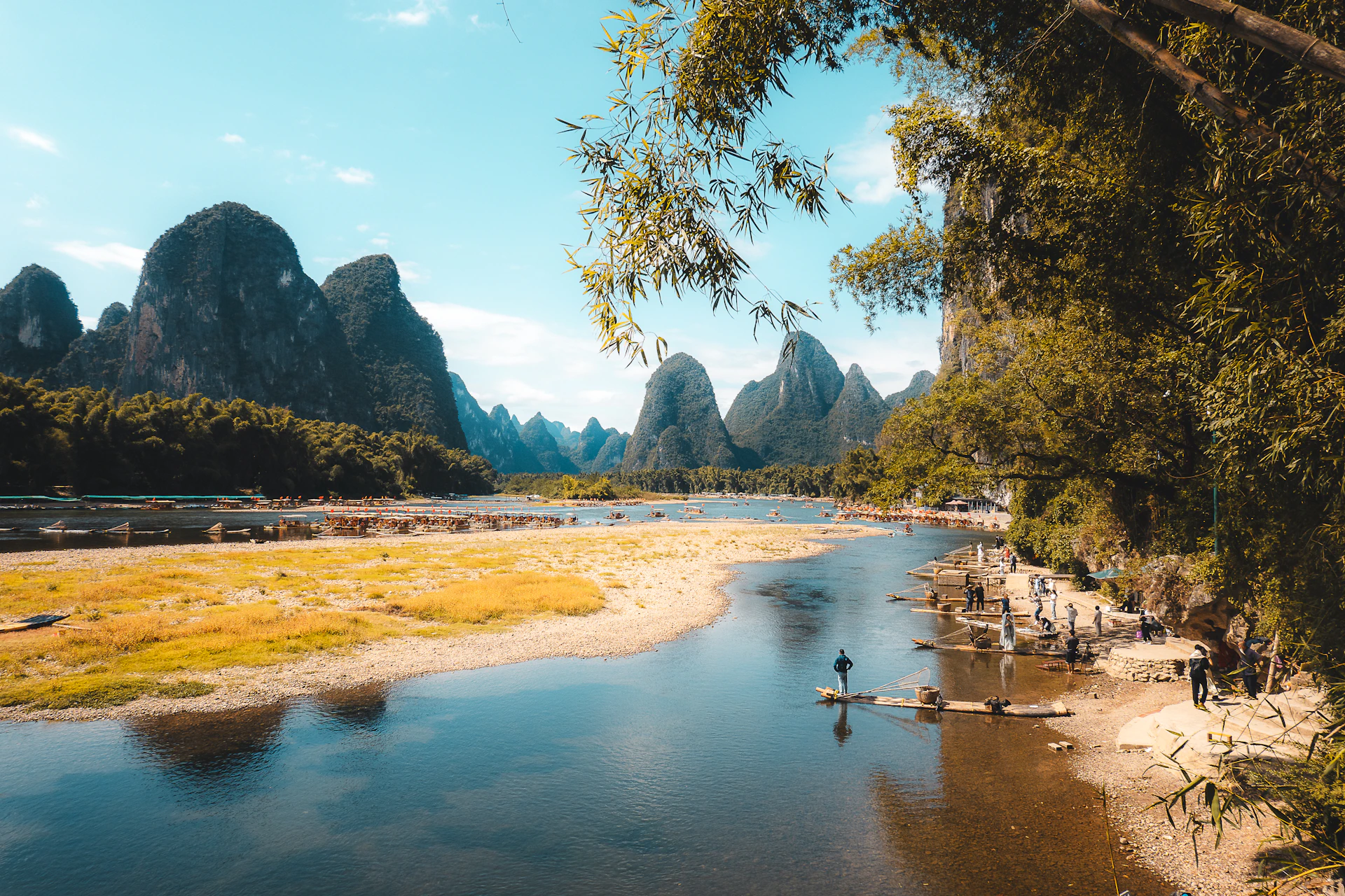 Karst mountains rise above a tranquil river with bamboo trees.