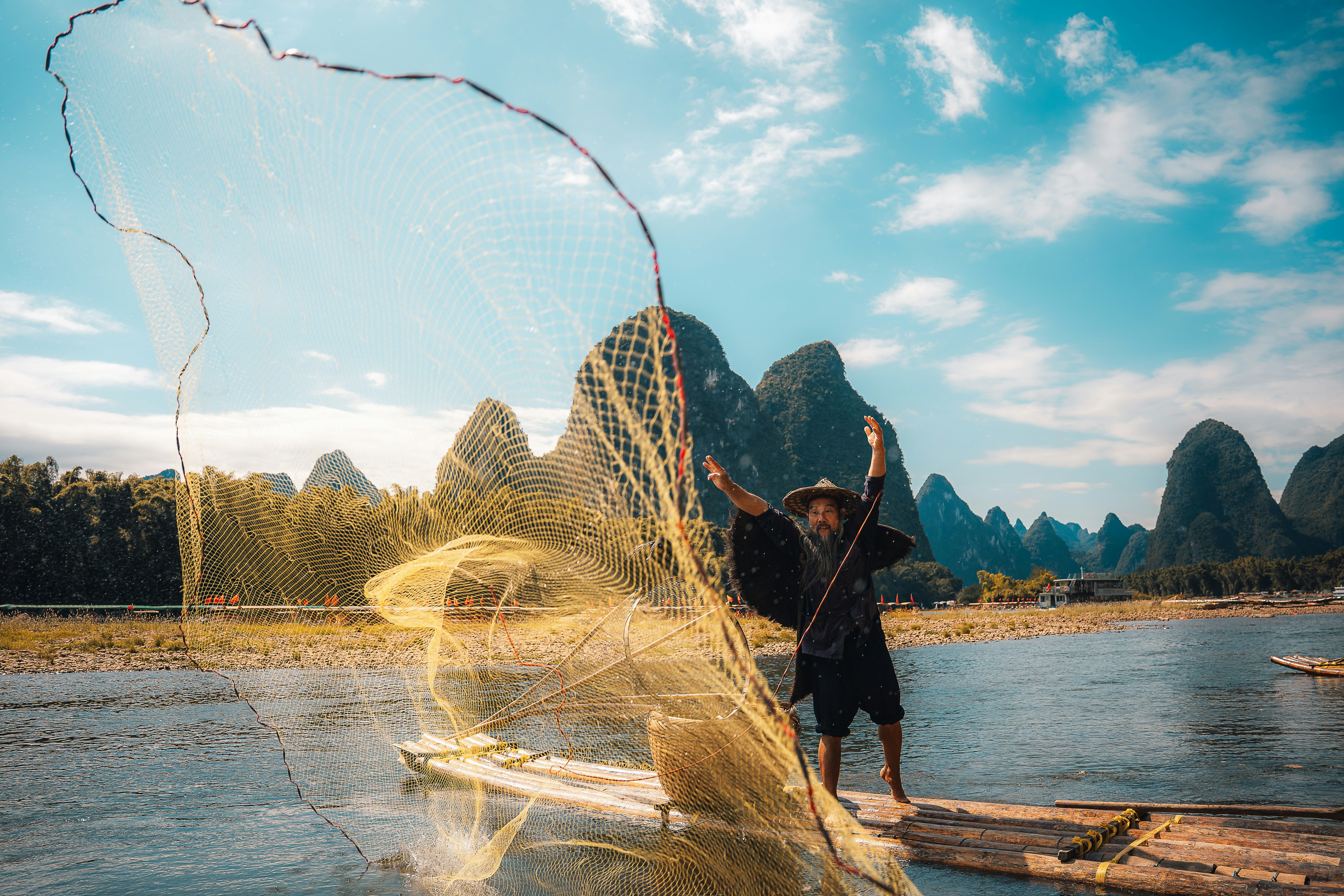 Fisherman casting a net from a boat on a river.