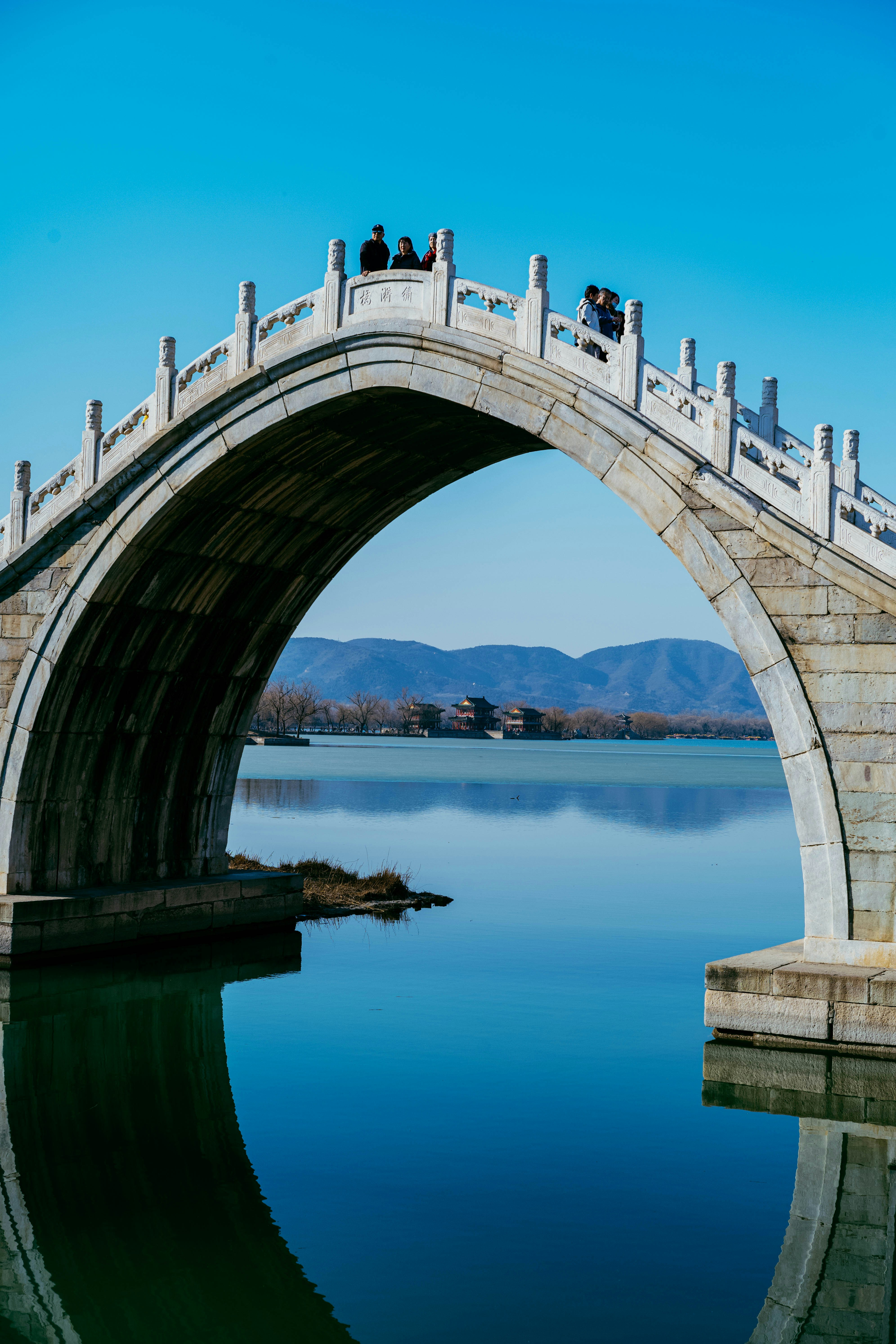 Pont voûté en pierre au-dessus d’une eau calme avec des montagnes lointaines.