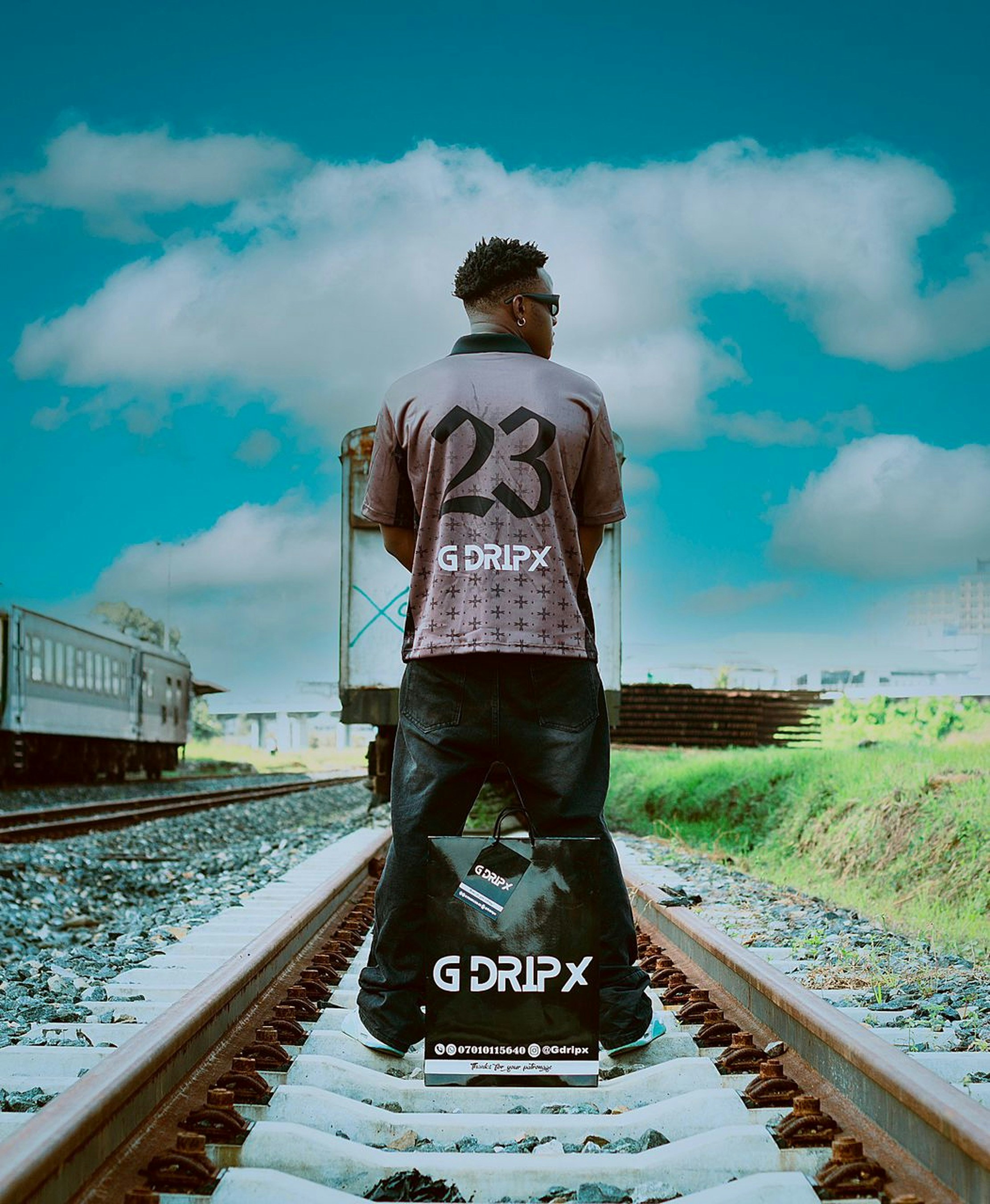 Man in '23' shirt stands on train tracks.