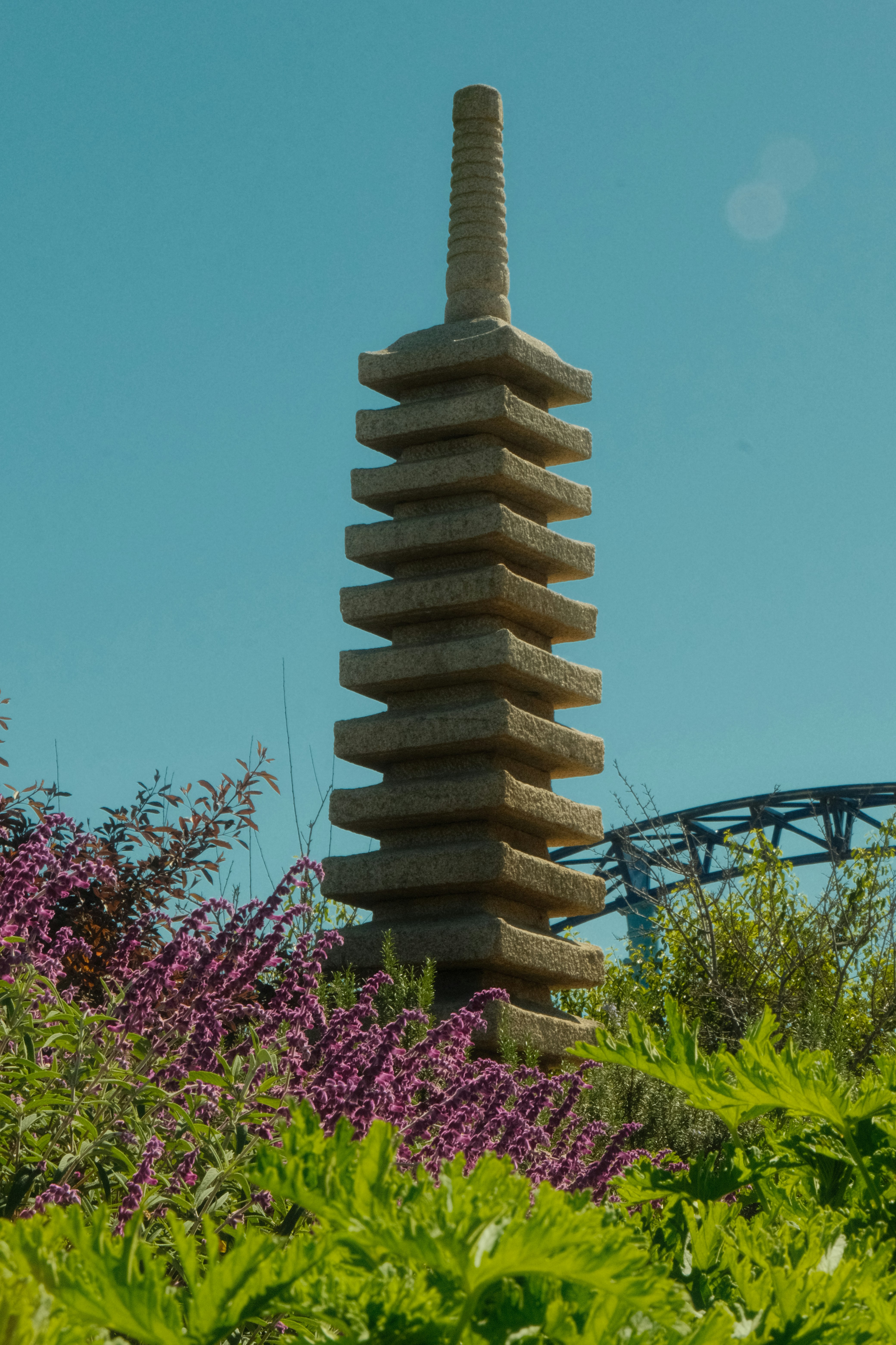 Stone pagoda surrounded by lush green plants and purple flowers.