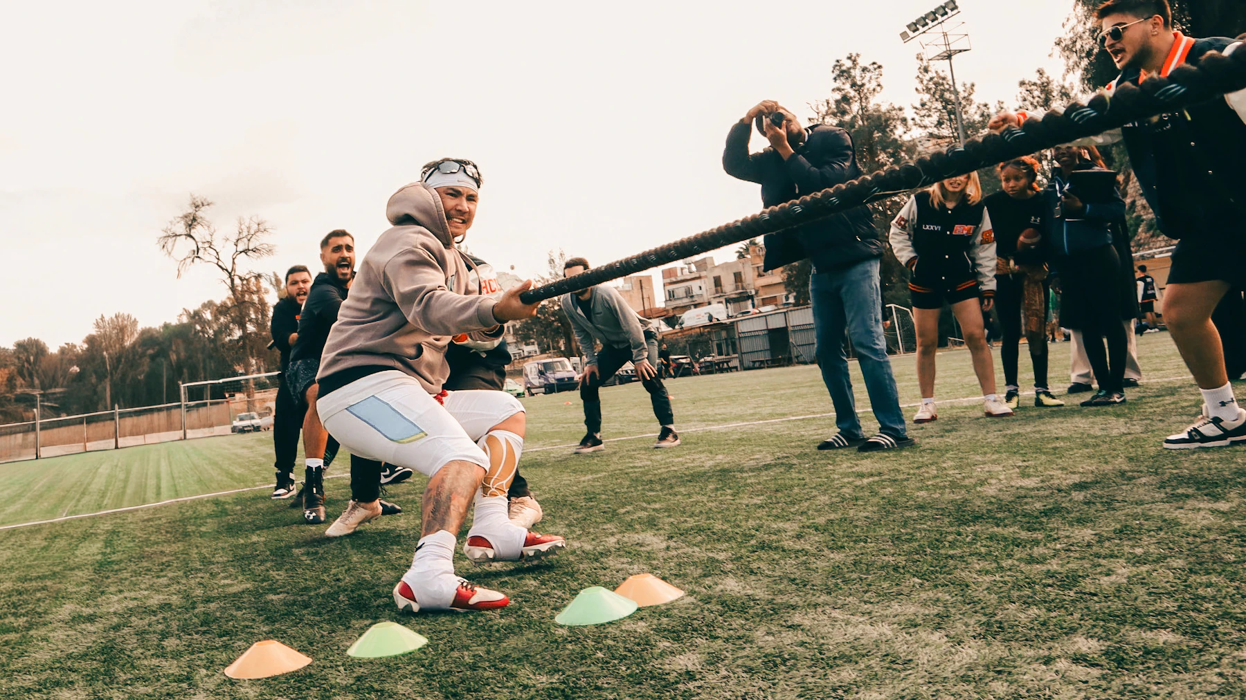 Two pullers leaning back on a taut rope beside a row of colored disc cones on a turf field