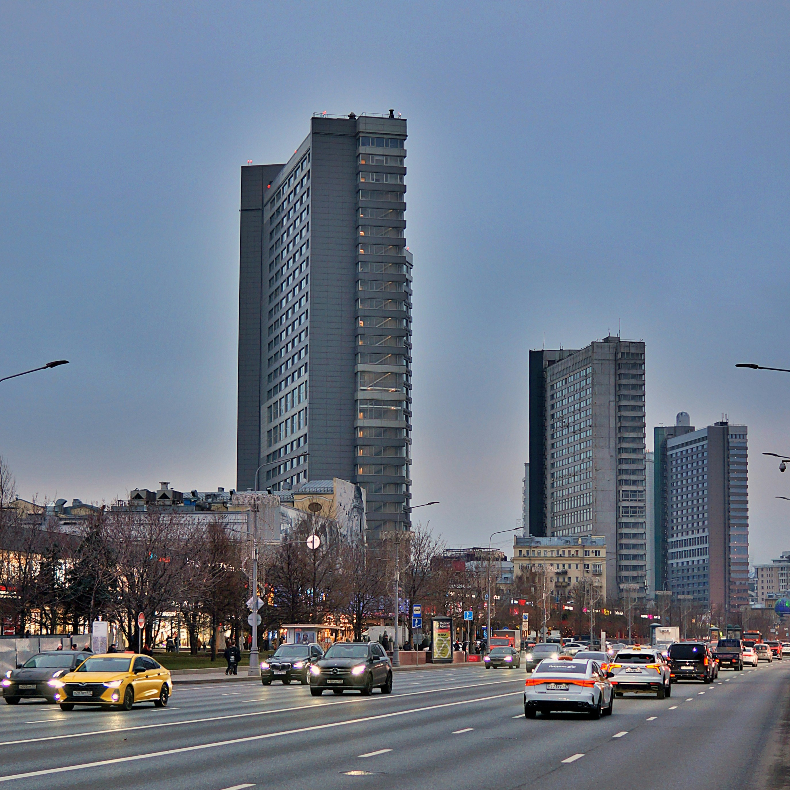 高層ビルが立ち並ぶ街の通りを走る車。
