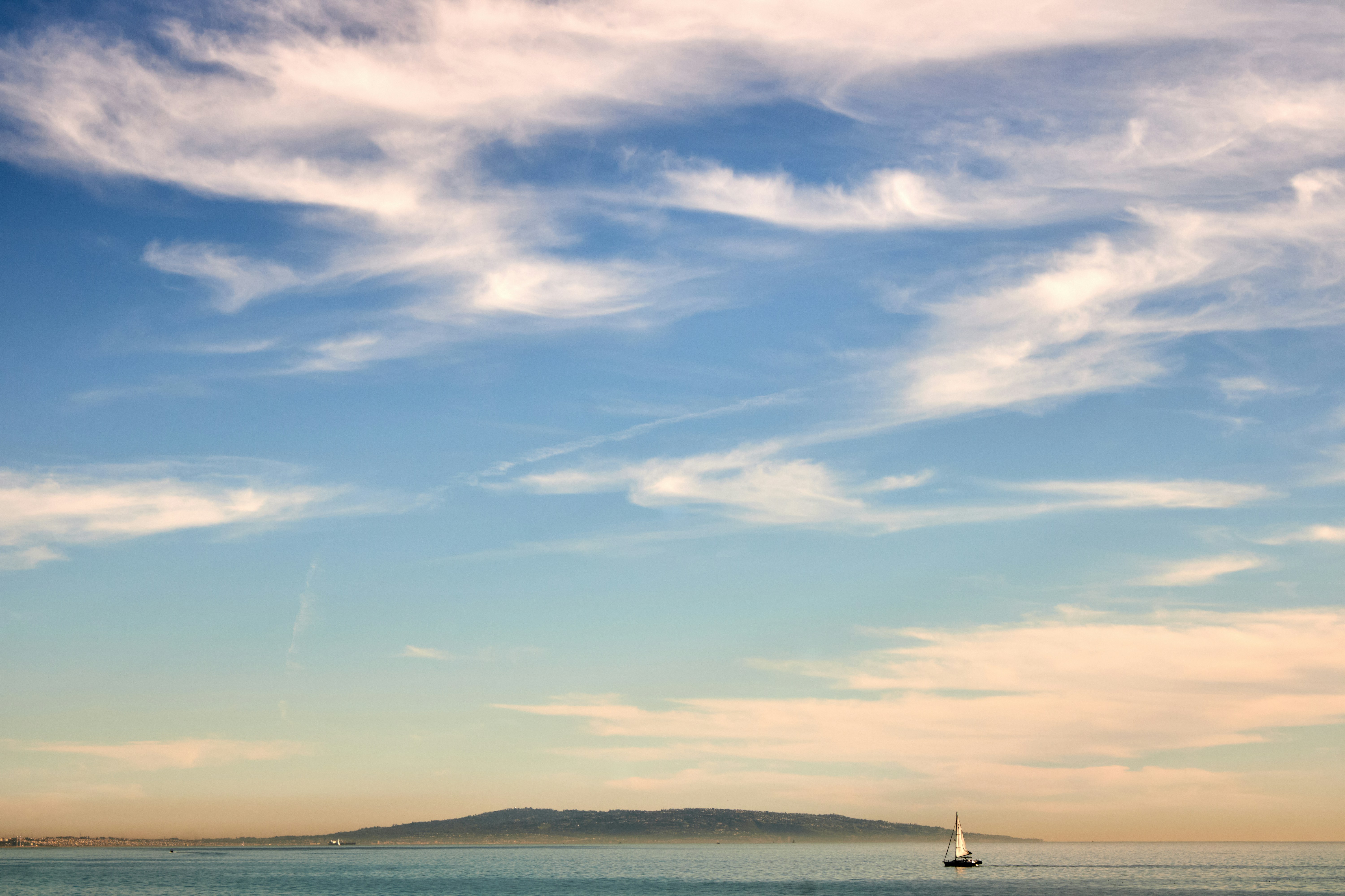 Golden sunset over Santa Monica Beach in Los Angeles, California. Peaceful Pacific Ocean horizon capturing classic West Coast coastal vibes. Minimalist single sailboat.