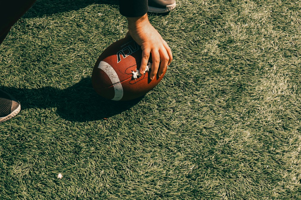 Un ballon de football américain tenu à la main au-dessus d’un terrain en herbe