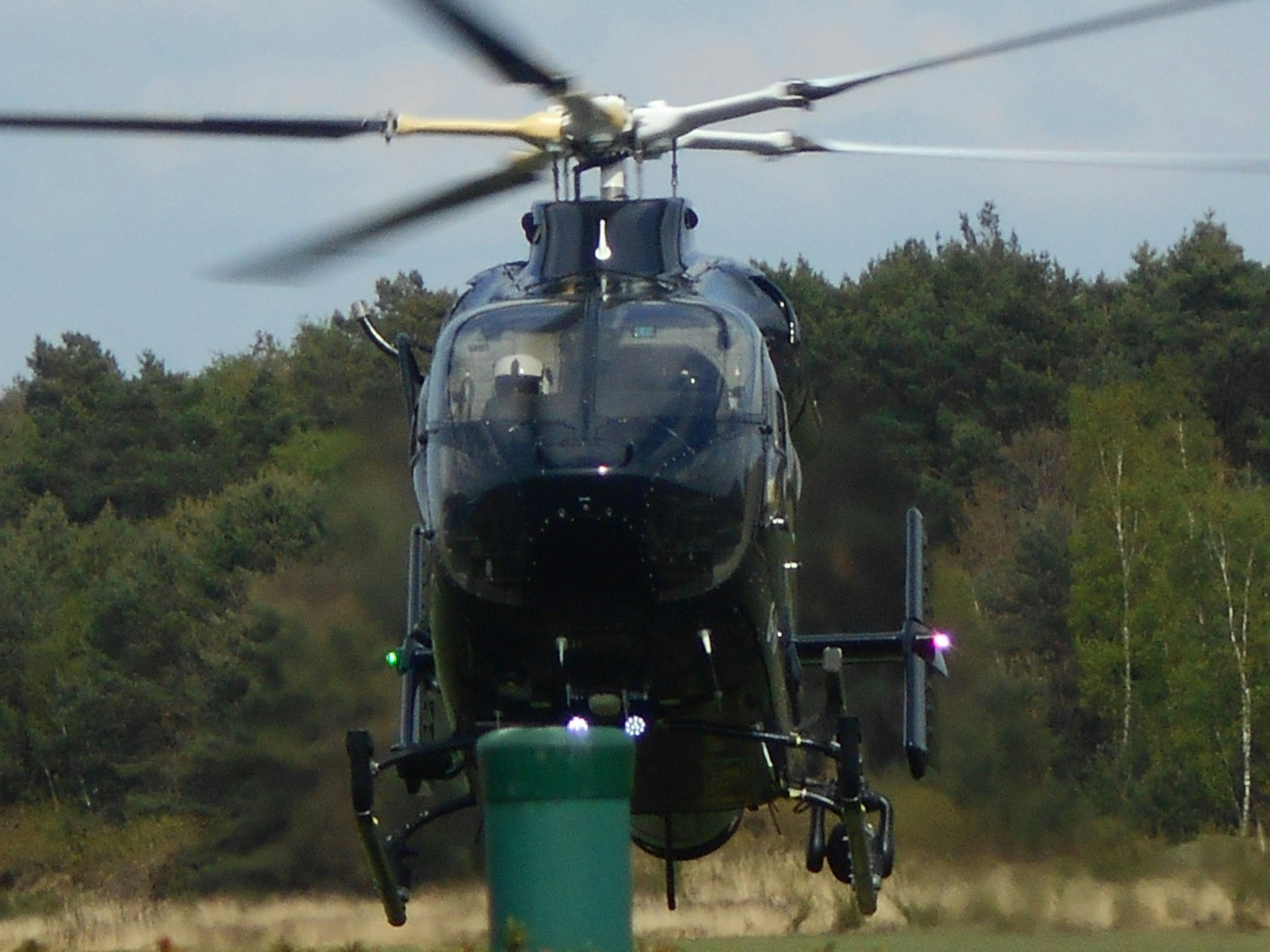 A dark helicopter hovers over a green object.