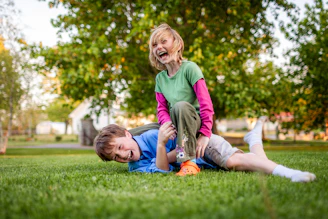 Two children laughing while playing on grass.