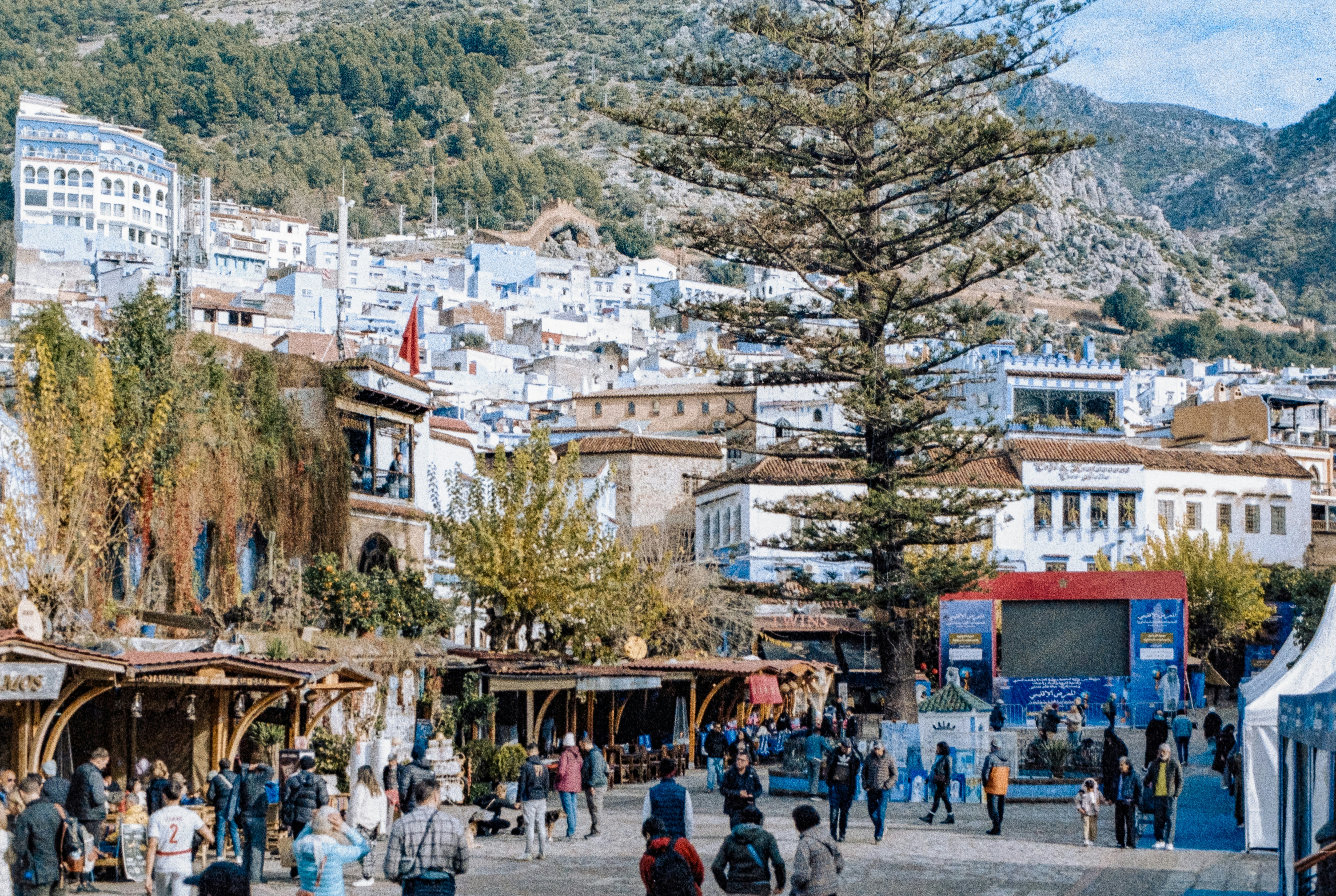People gather in a bustling town square with blue buildings.