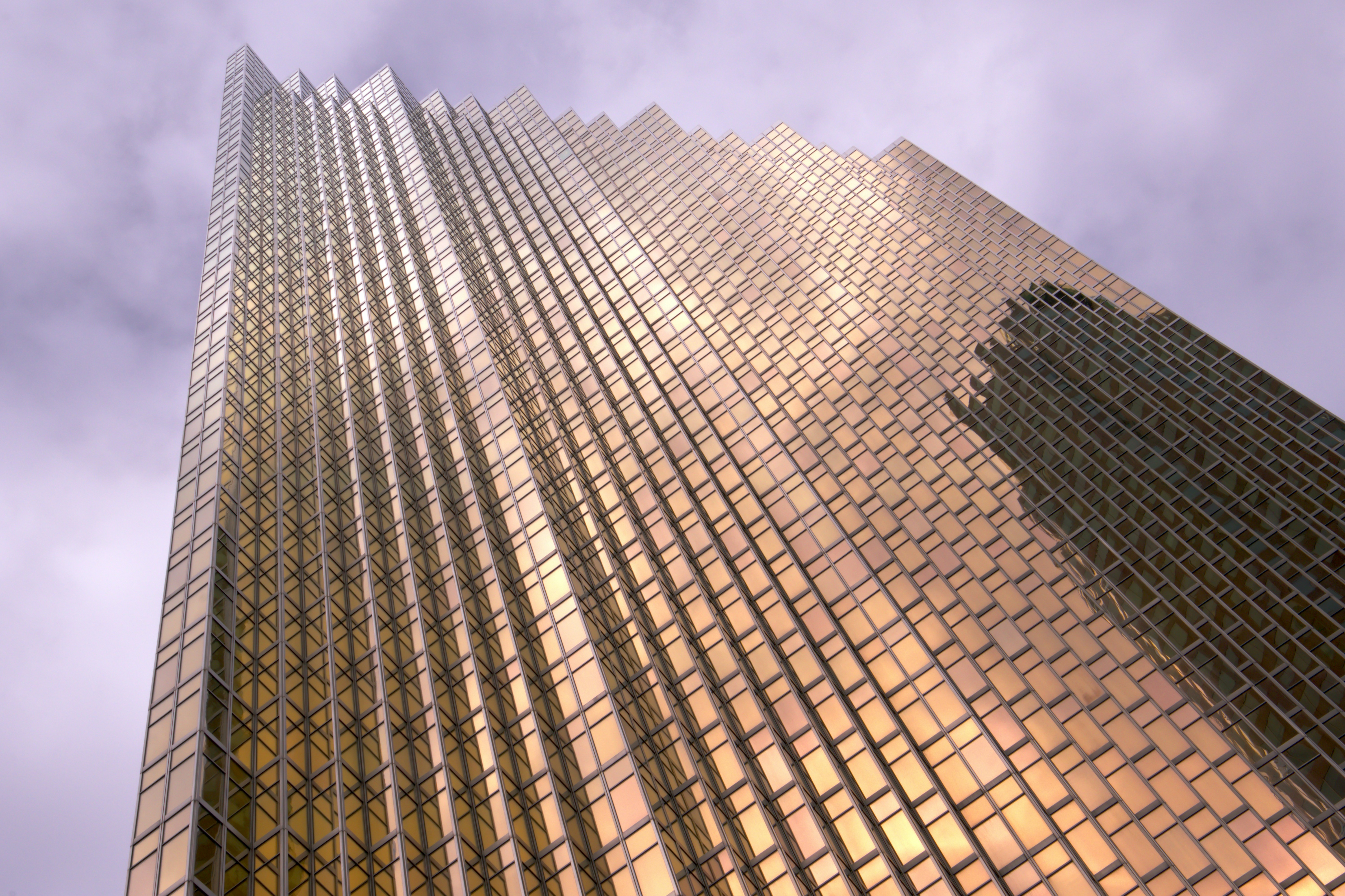 Rascacielos dorado con fachada de cristal contra cielo nublado.