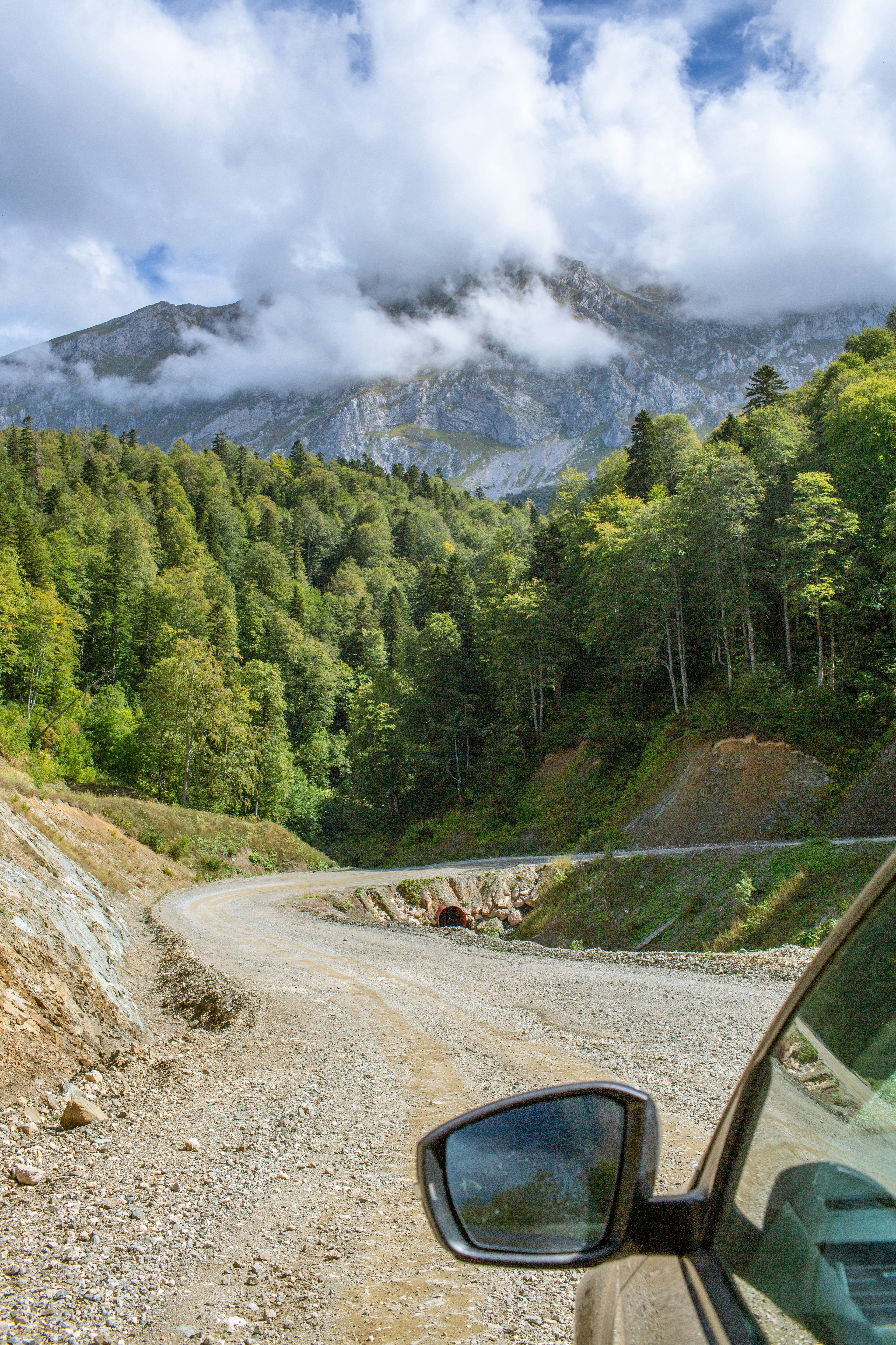 Strada sterrata tortuosa attraverso montagne verdi e rigogliose sotto le nuvole.