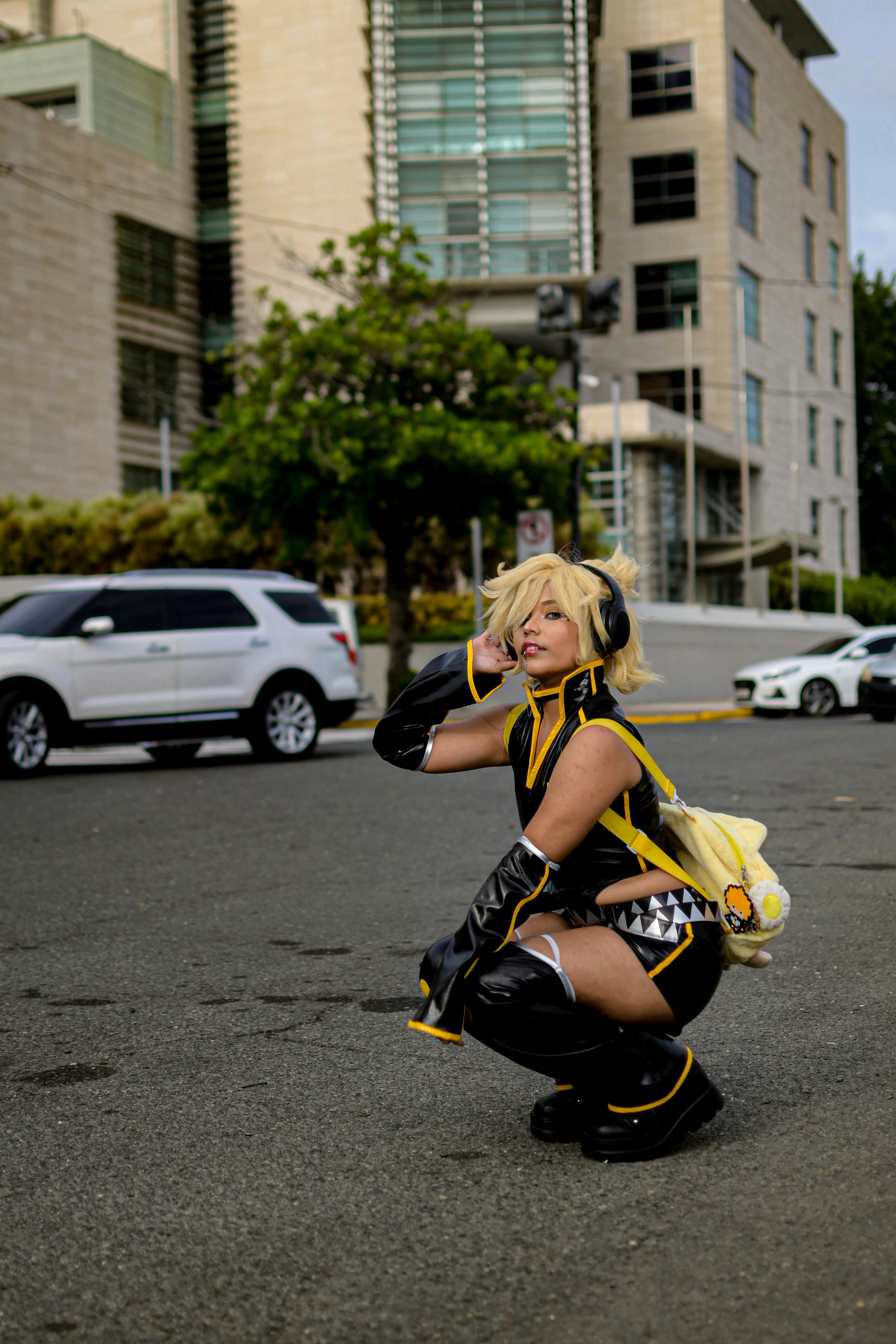 Cosplayer berpakaian kuning dan hitam berjongkok di jalan.