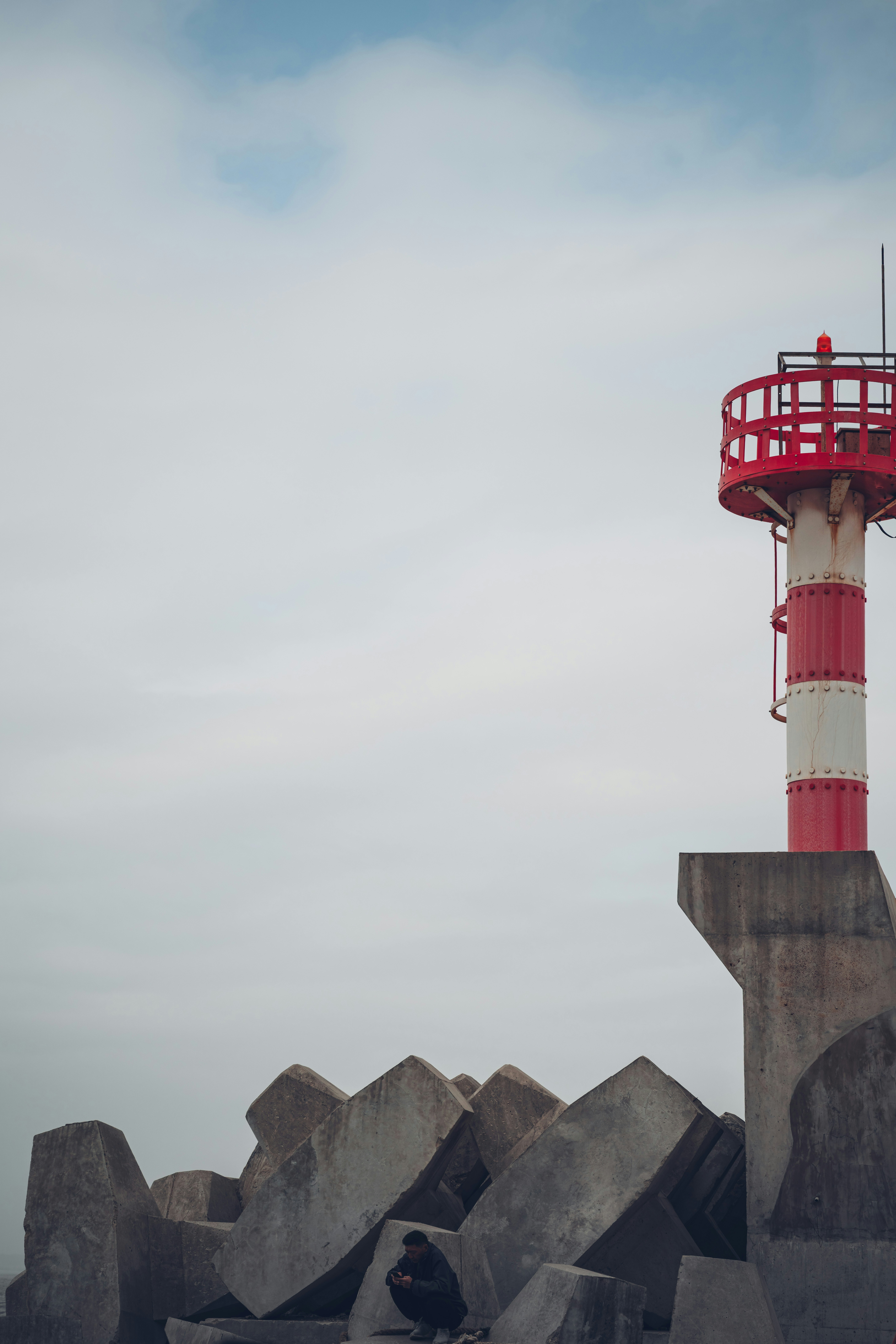 Un faro se alza junto a una persona sobre bloques de hormigón.