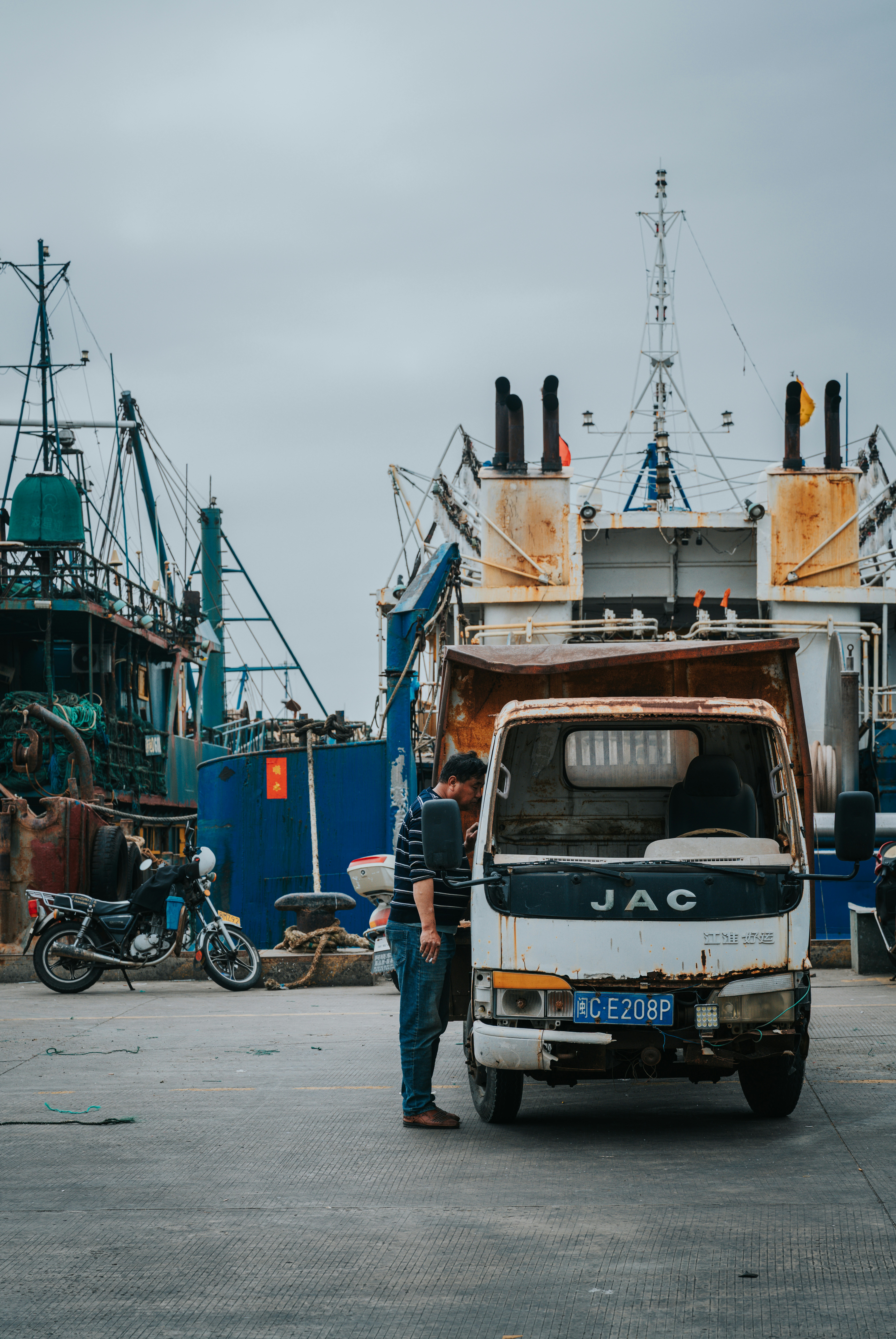 Hombre apoyado en un camión oxidado en un puerto