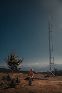 Person stands near a tall tower in a rural landscape.