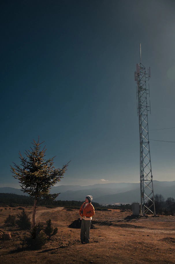 Person stands near a tall tower in a rural landscape.